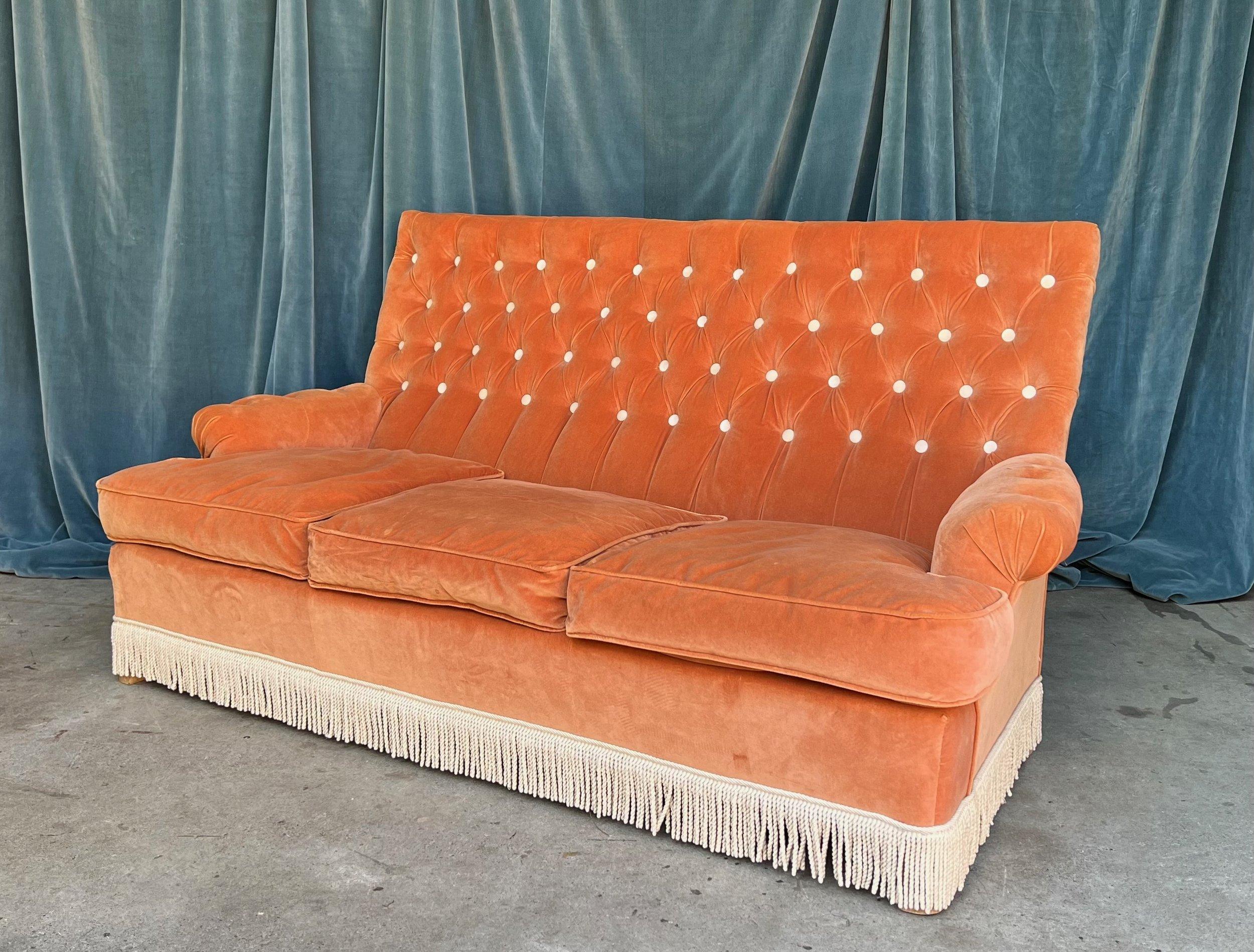This stunning French high-back sofa, designed in the opulent Napoleon III style, is the embodiment of luxury and elegance. Upholstered in a pale orange tangerine velvet, the back and arms of the sofa feature a diamond tufting pattern, emphasized by
