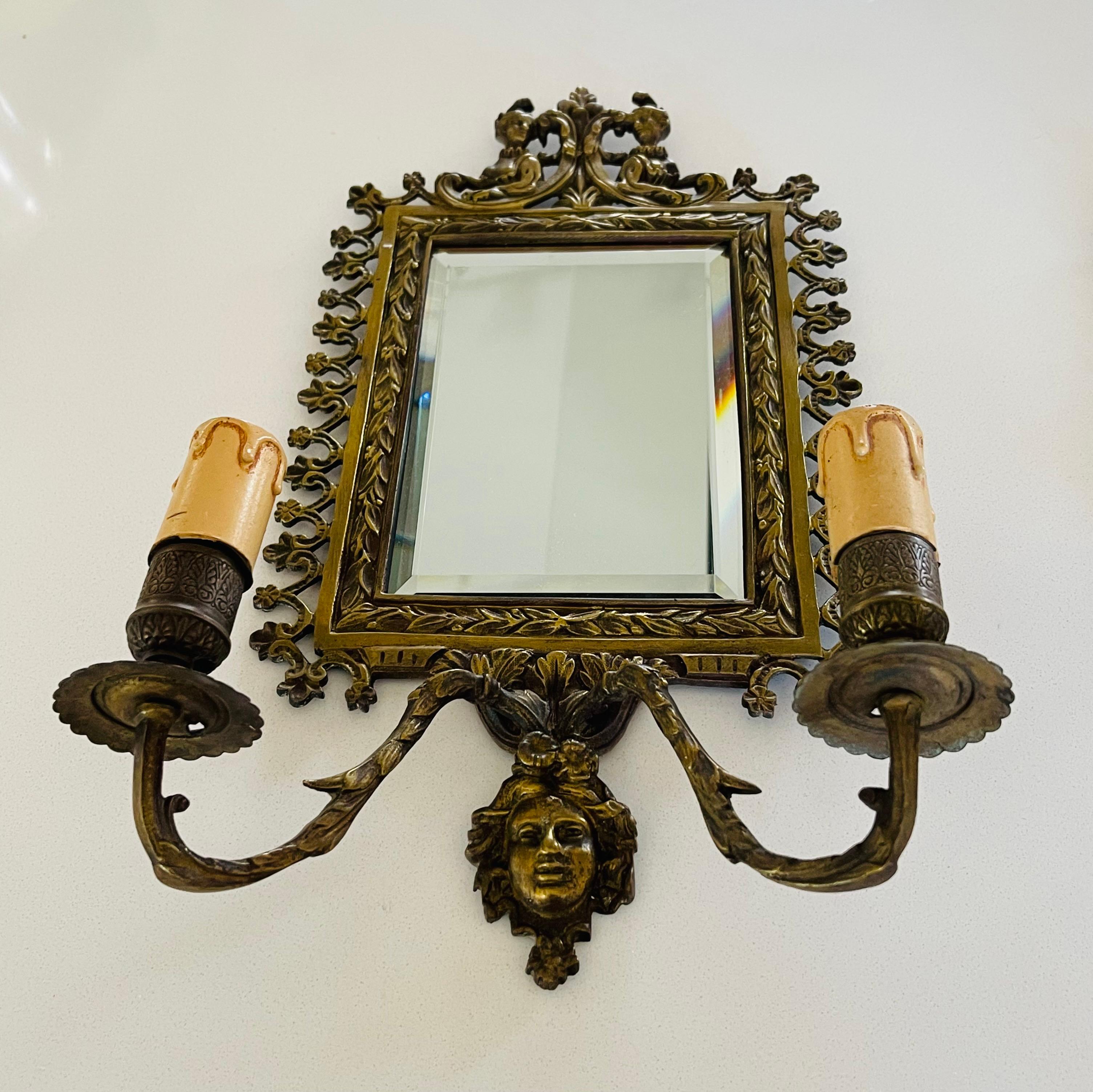 Pair of Napoleon III style bronze sconces. Bevelled mirror, two branches of lights. The bronze is worked and decorated with two women on the upper part of the cornice, and a face on the lower part.