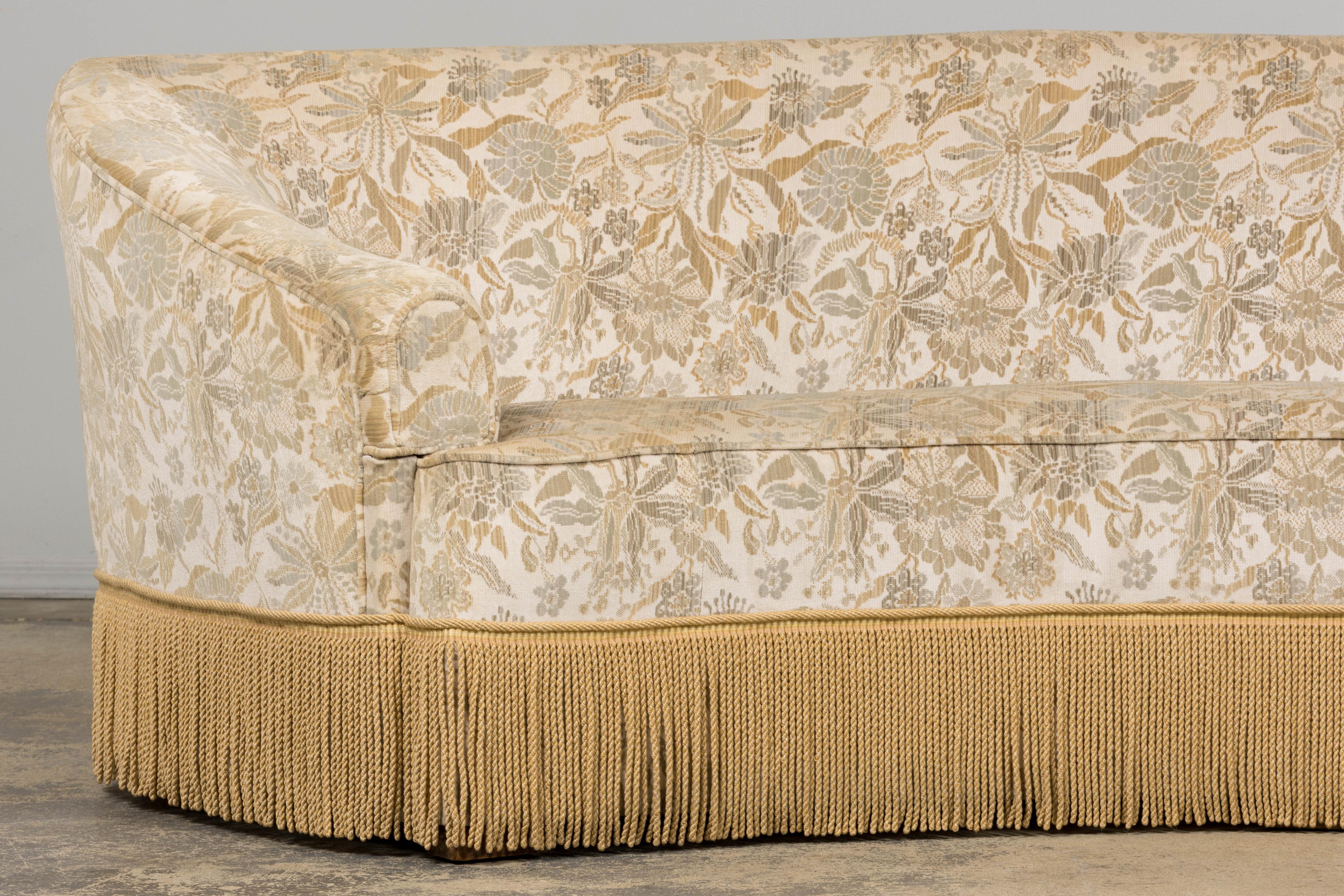 An exquisite French mid-20th century curved sofa in the style of Napoleon III, sourced in Provence, France. The solid wooden frame is crafted in a graceful crescent form with a continuous back and sweeping arms. Upholstered in a floral jacquard