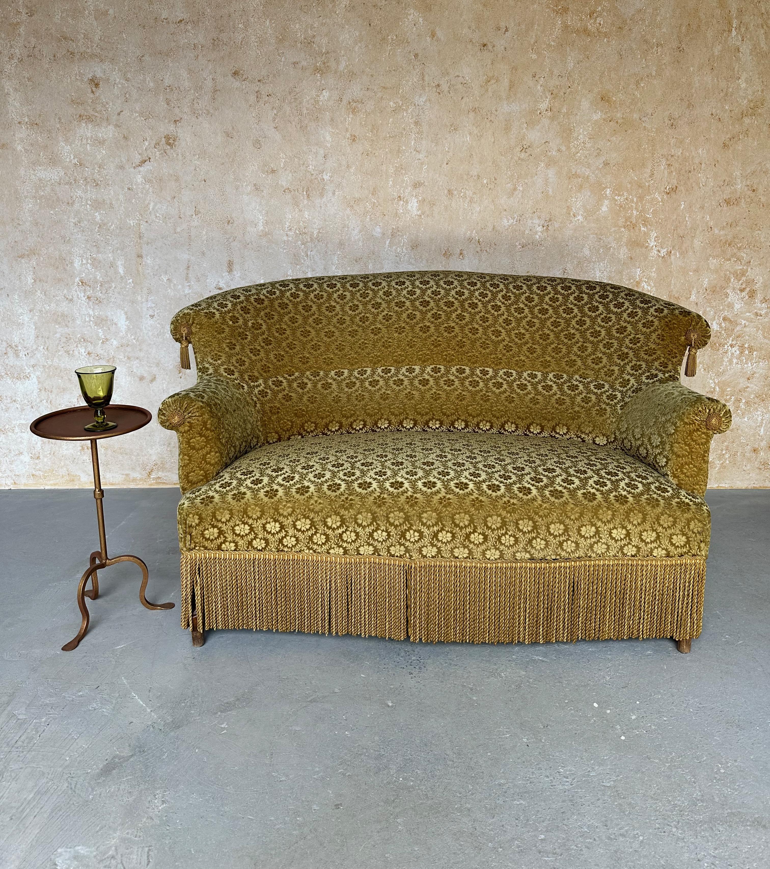Questo elegante divano francese in stile Napoleone III è rivestito in velluto dorato a motivi floreali con ornamenti di nappe e frange in tinta. Lo schienale splendidamente curvo e il supporto lombare incorporato, tipici delle sedute Napoleone III,
