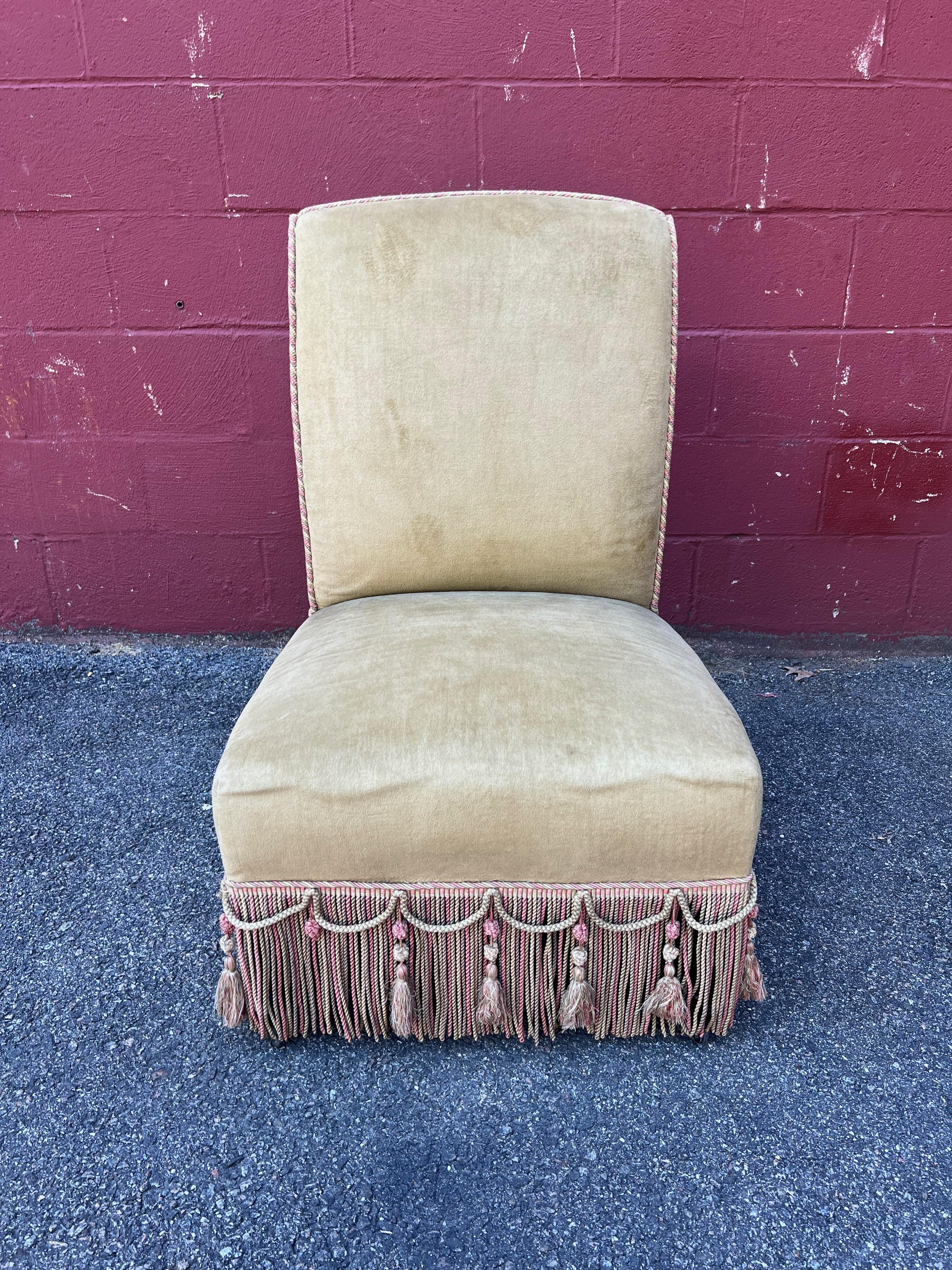 An outstanding large scale French 1920s Napoleon III style slipper chair. This slipper chair is truly magnificent. It is upholstered in a delightful pale tan velvet, and is ornamented with multicolored bullion fringe and tassels for added luxe
