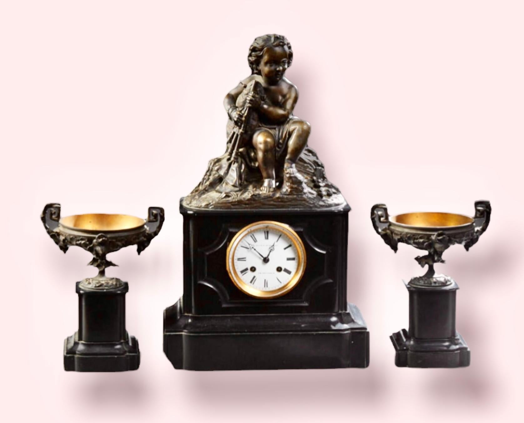 An outstanding Antique French Napoleon III three piece bronze and marble clock garniture set, c. 1880, with a bronze surmount of a putto playing a bagpipe, over a drum clock, time and strike, with an enamel dial on a sloping stepped base; together