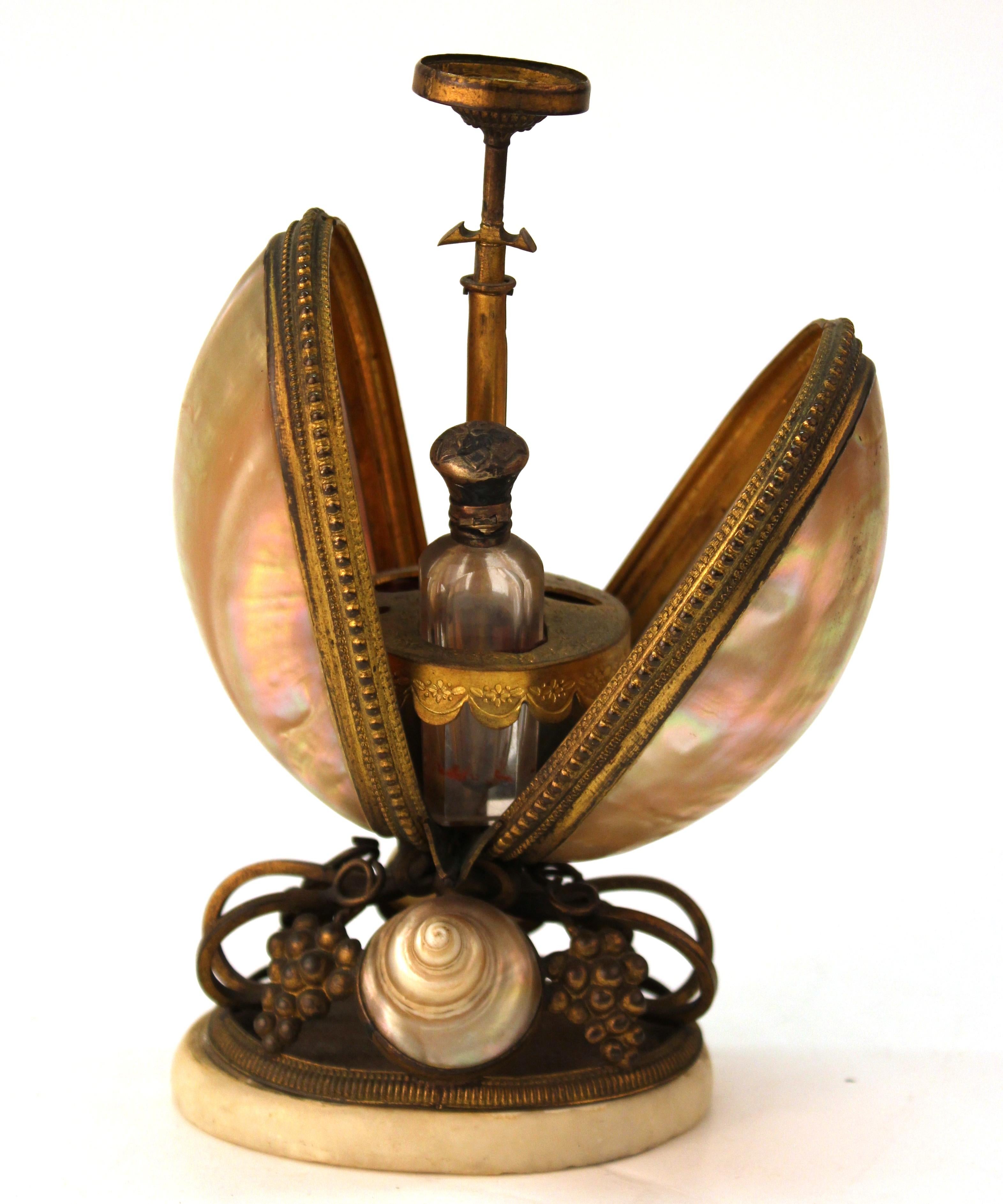 French nautilus shell and ormolu gilt metal mounted egg-shaped mechanical holder, with the egg opening and revealing a perforated stand housing an antique perfume or smelling salts bottle. The piece is lacking the top shell and some interior