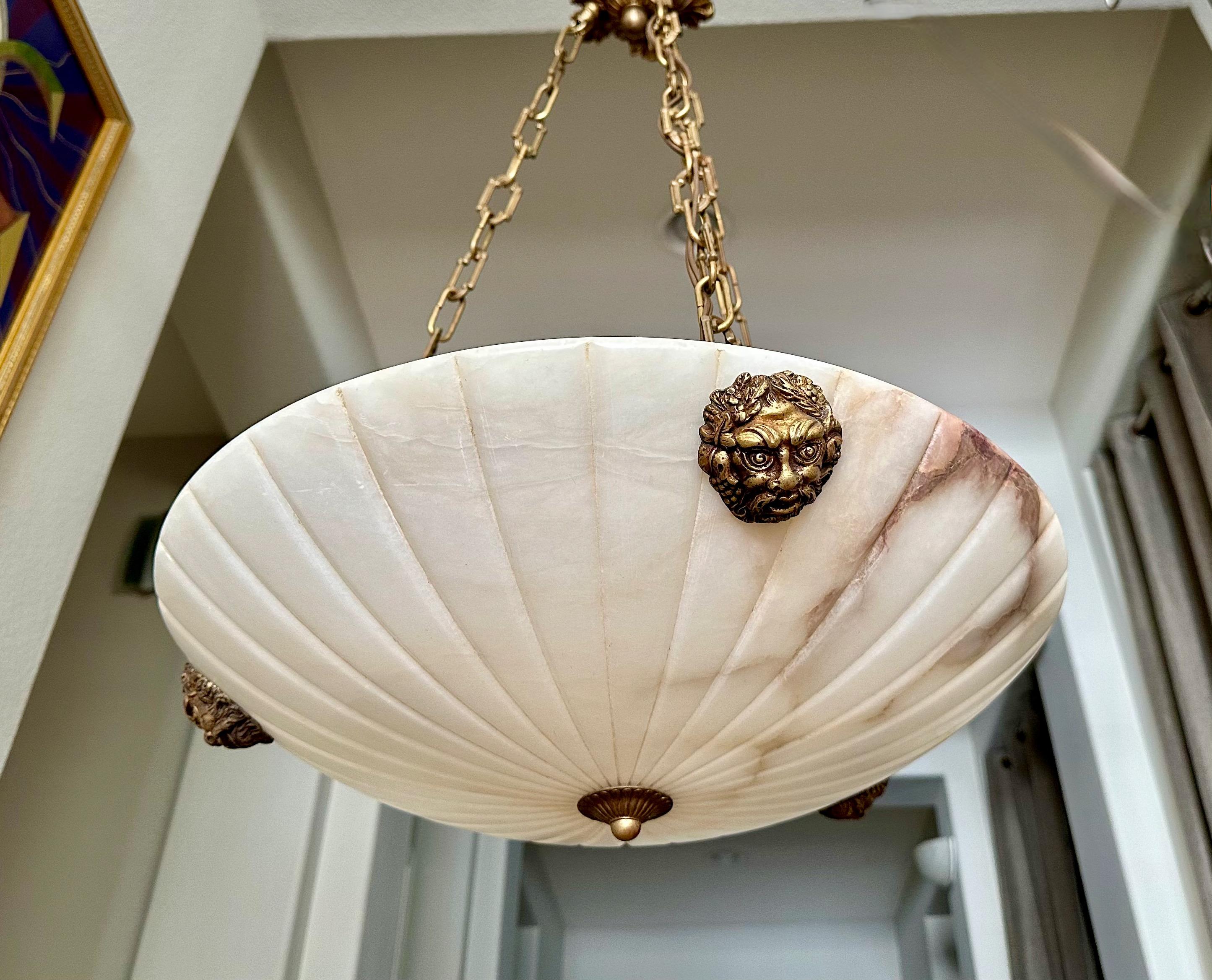 French neoclassic style alabaster chandelier pendant light with aged brass fittings including Bacchus head escutcheons. The white Alabaster has lots attractive natural brown tone veining. The Interior lighting uses 3 60-watt intermediate base bulbs