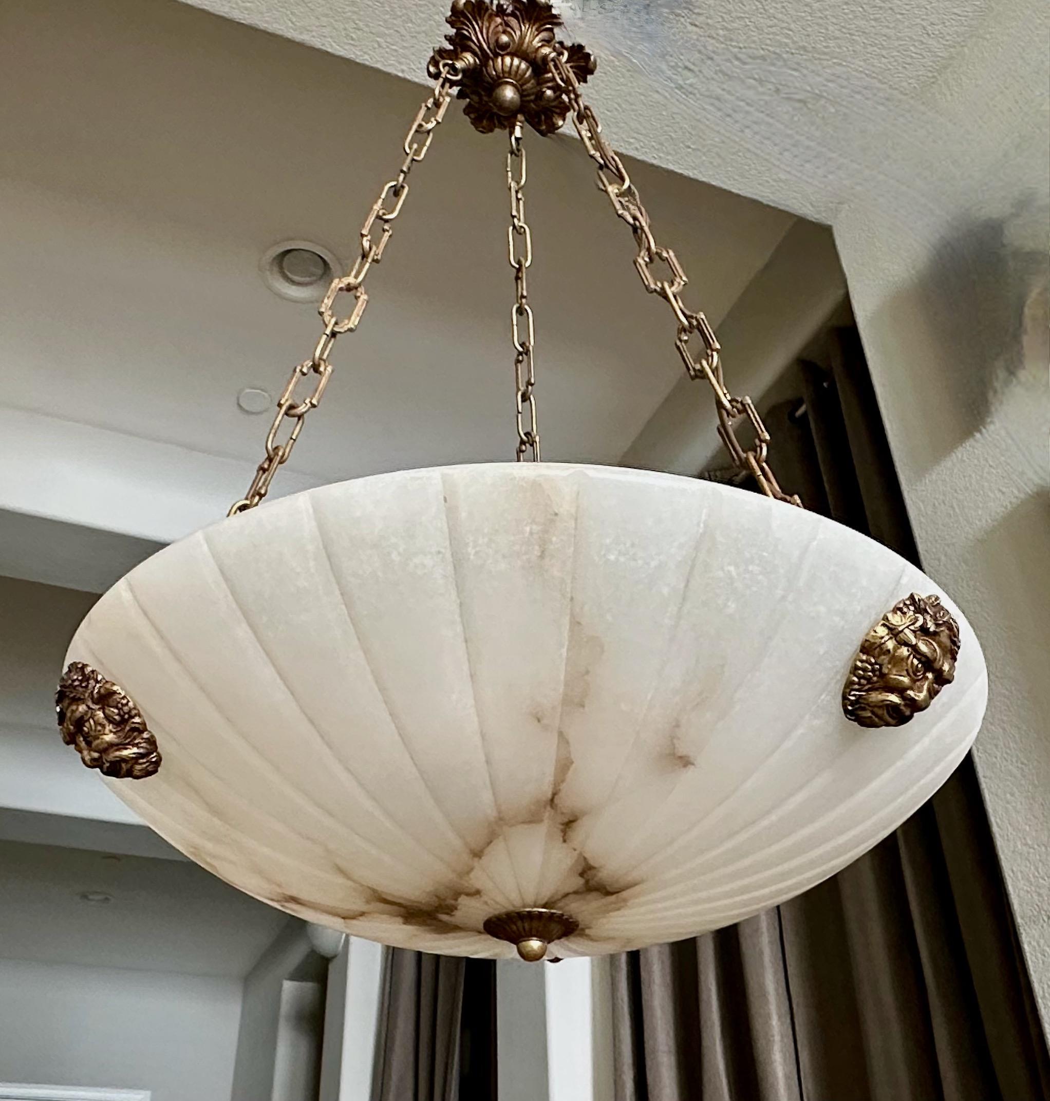 French neoclassic style alabaster chandelier pendant light with aged brass fittings including Bacchus head escutcheons. The white Alabaster has lots attractive natural brown tone veining. The Interior lighting uses 3 60-watt intermediate base bulbs