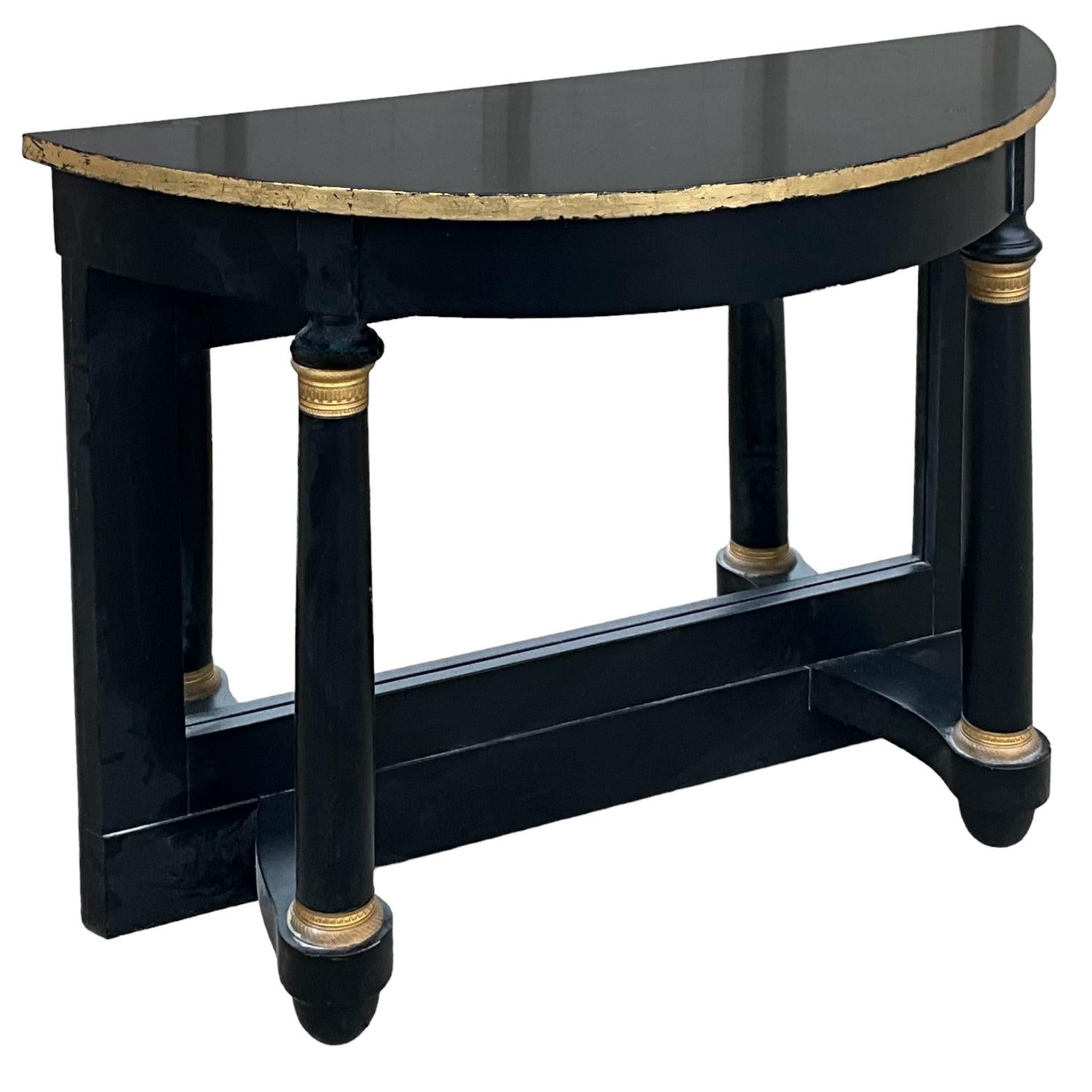 This is a pair of French neo-classical style black lacquered console tables by Maison Jansen. The backs are mirrored. Each turned support is banded in gilt bronze. The demilune topes are leafed in gold. They are marked and in very good