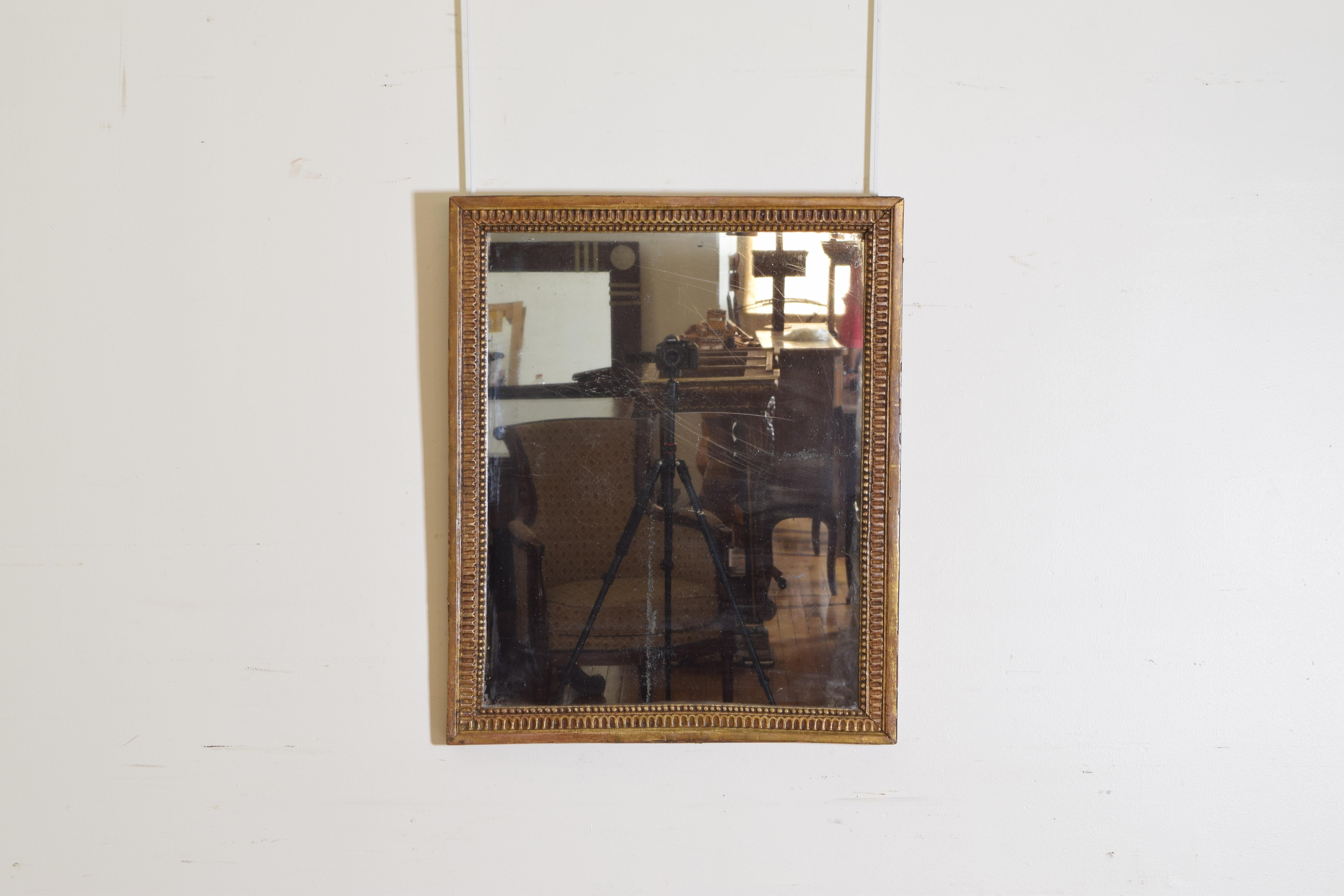Having a dentile and bead carved giltwood frame and retaining its original mirror plate.