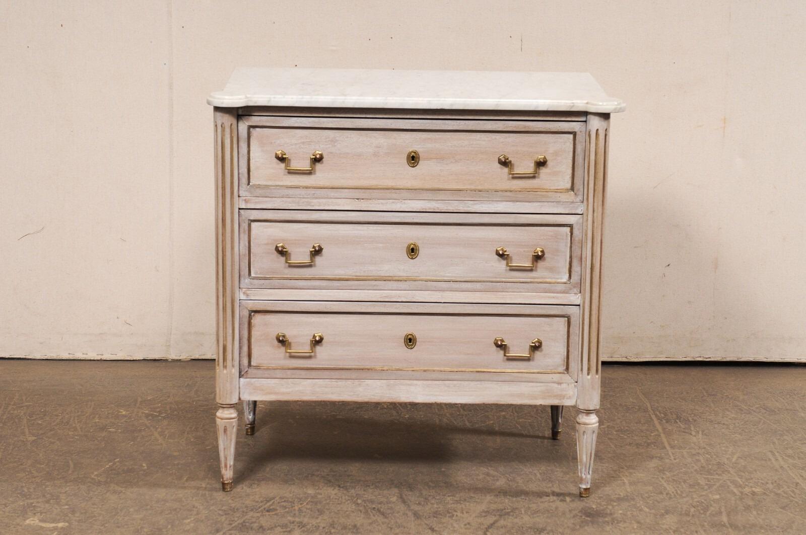 A French Neoclassical-style carved wood chest of drawers with marble top. This vintage chest from France, designed in Neoclassical fashion, features a rectangular-shaped white marble top with pronounced and rounded front corners, that rests atop a