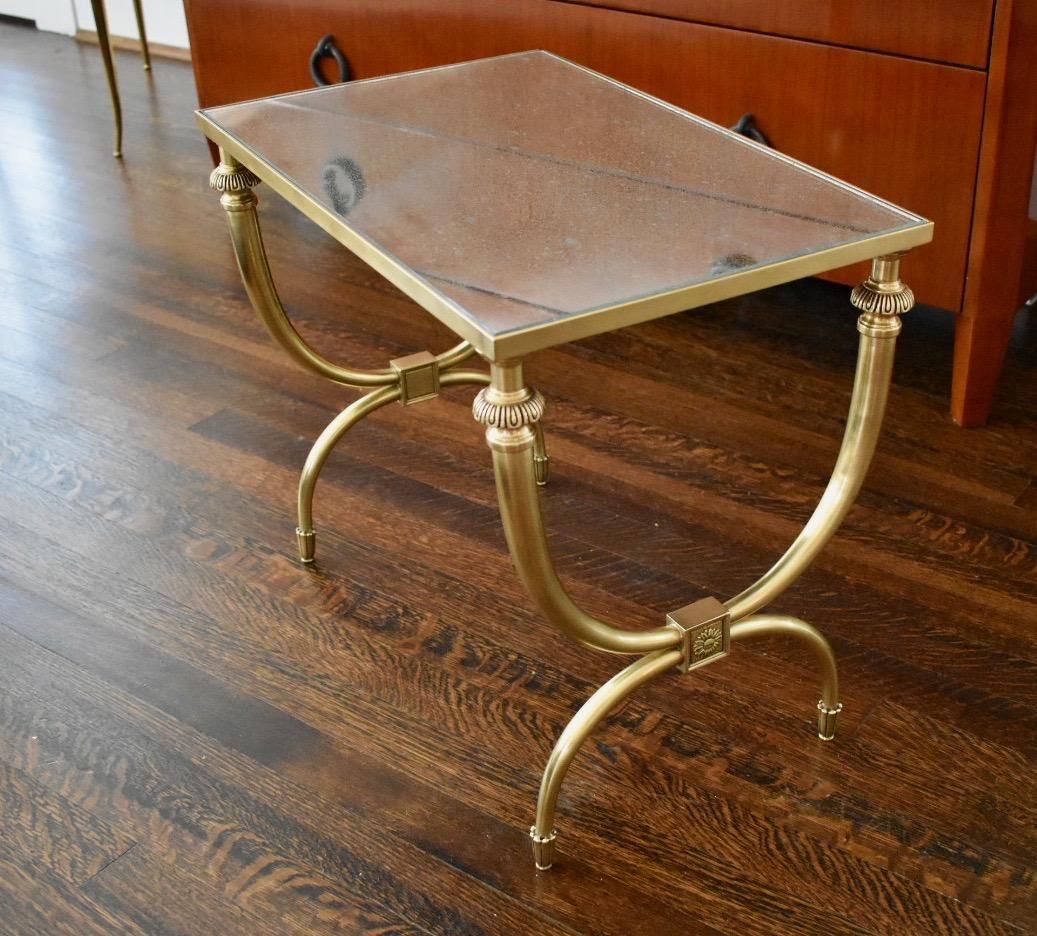 French or Italian curule form brass side or end table. Inset mirrored glass top has a beautiful patina to silvered backing. Warm golden patina to brass accents details to table. A steel 