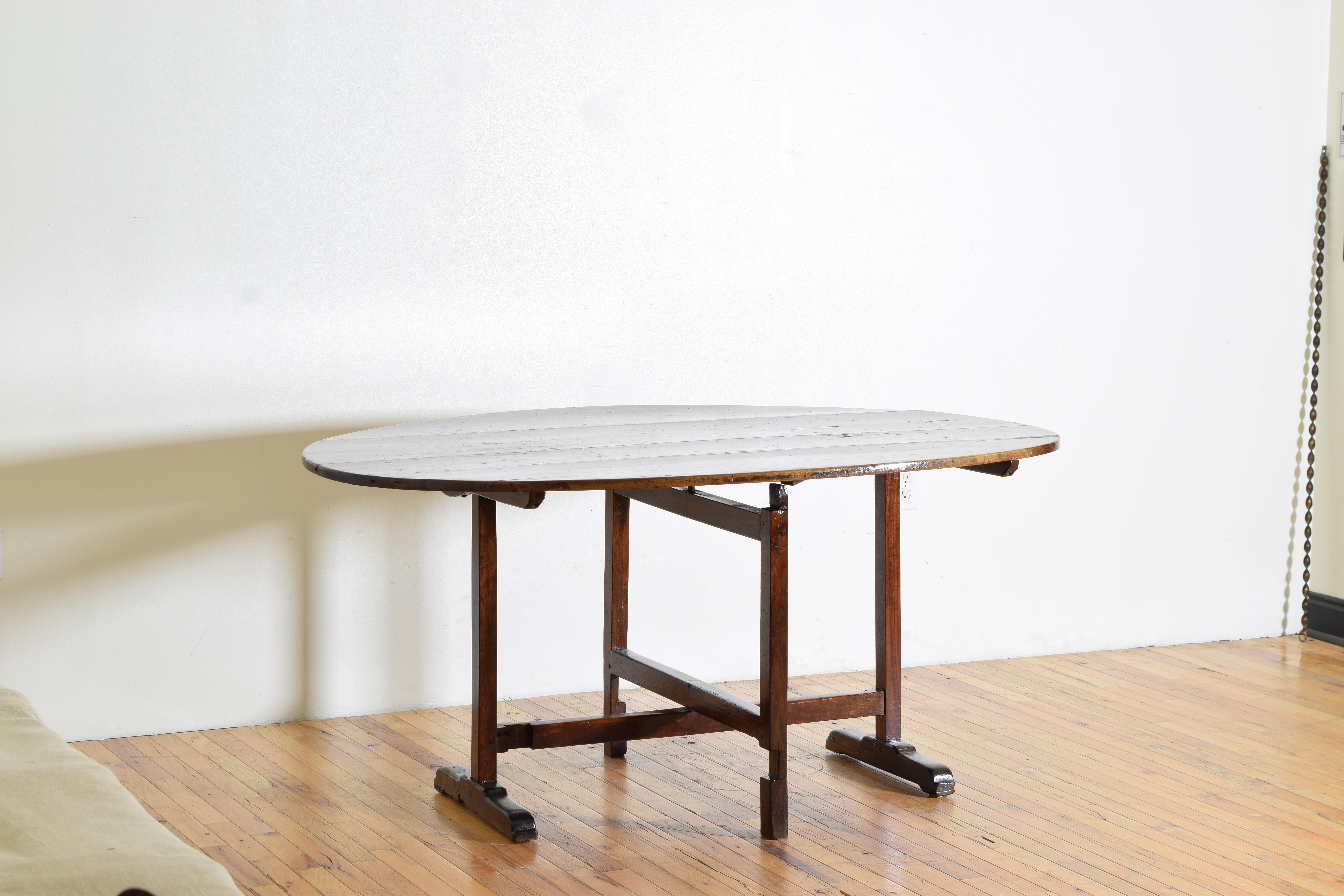 a portable table taken by wagon to the grape harvest in vineyards often used for meals and work this model is a large oval, the top of beautifully figured walnut boards, the swivel base locking at perpendicular to support the top, the square legs
