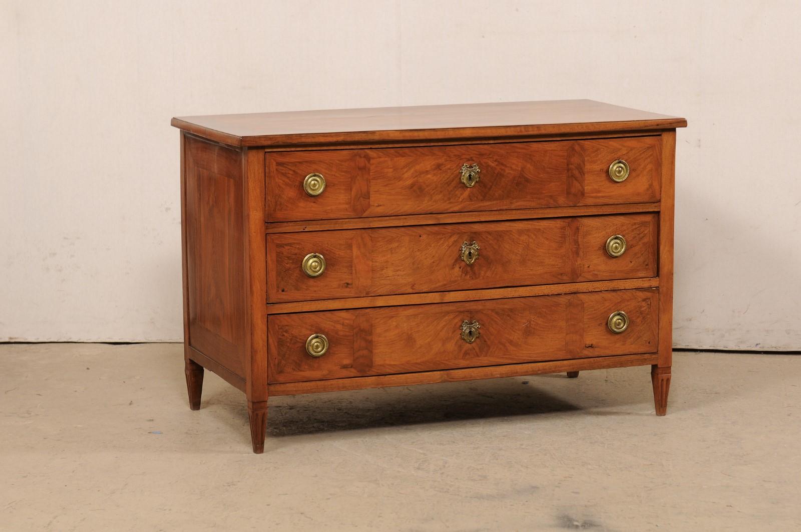 A French neoclassical commode, with lovely veneer inlays, from the early 19th century. This antique chest from France features a rectangular-shaped top with exquisite book-match veneer top over a case which houses three full-sized and graduated