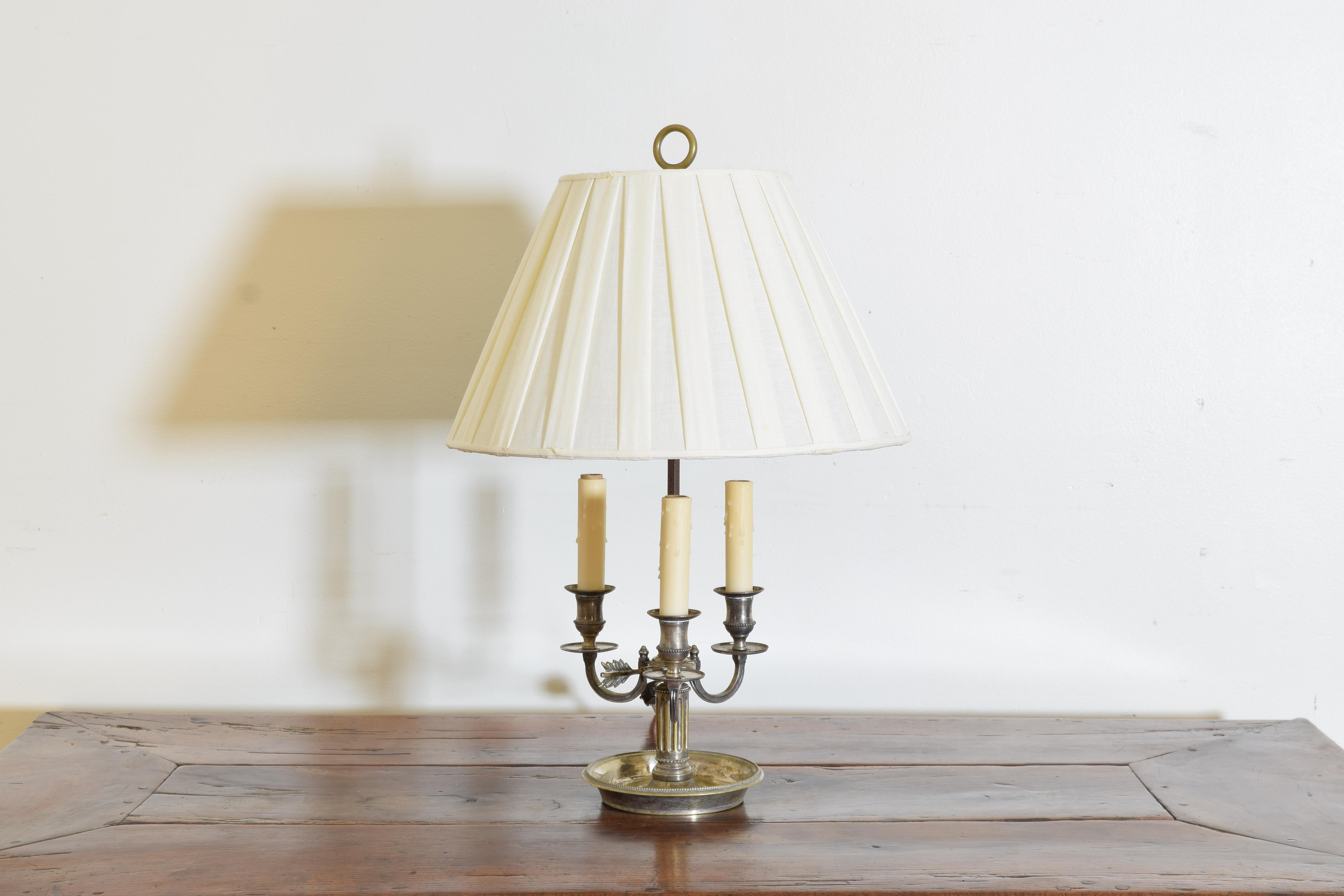 Having a fluted standard issuing three curved arms, the standard atop a circular tray, with silk lampshade, height measured is to top of shade, height  to top of candles is 11 inches, diameter is of lampshade