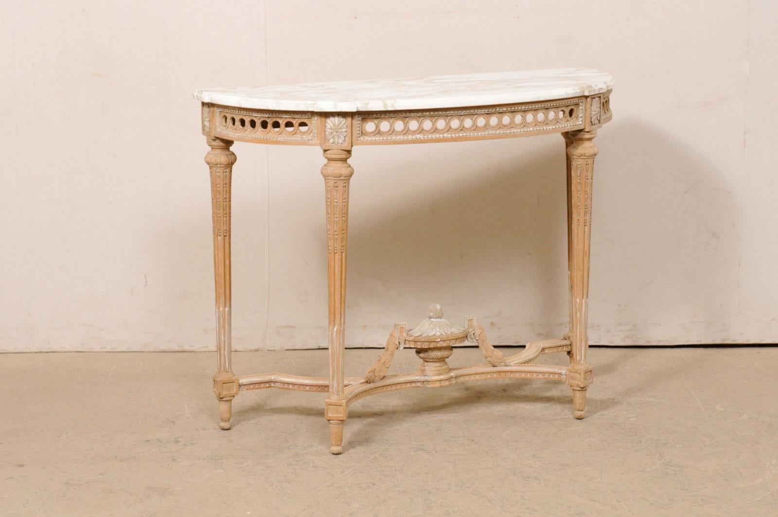A French Neoclassic style marble-top console, with carved urn finial accent at underside, from the mid 20th century. This vintage table from France features an oblong-demi shaped white marble top, with shallow stepped out accents above each leg. The