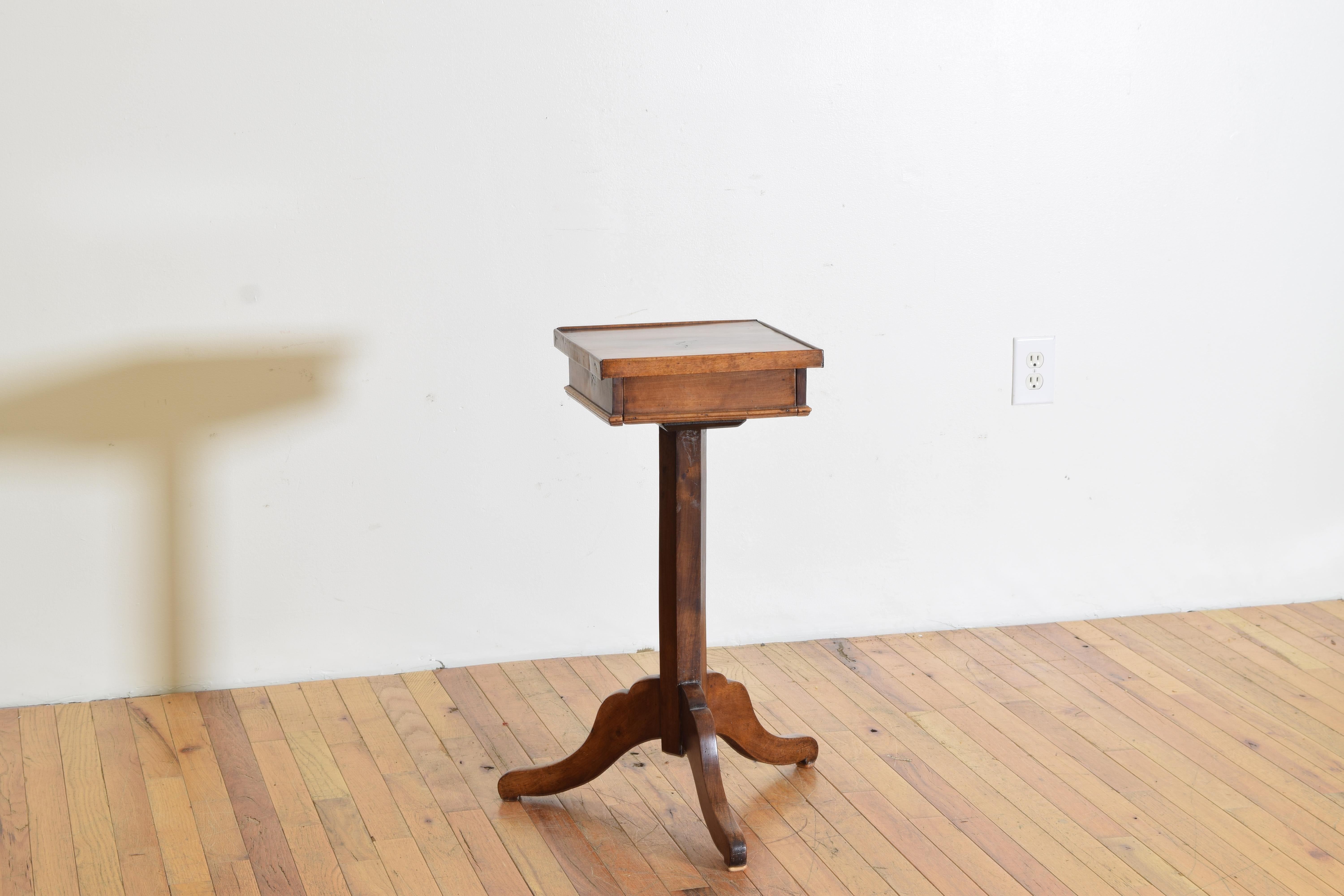 Having a square top with a slightly raised gallery, the top concealing a single drawer, raised on a hexagonal standard atop a tripartite base with shaped feet