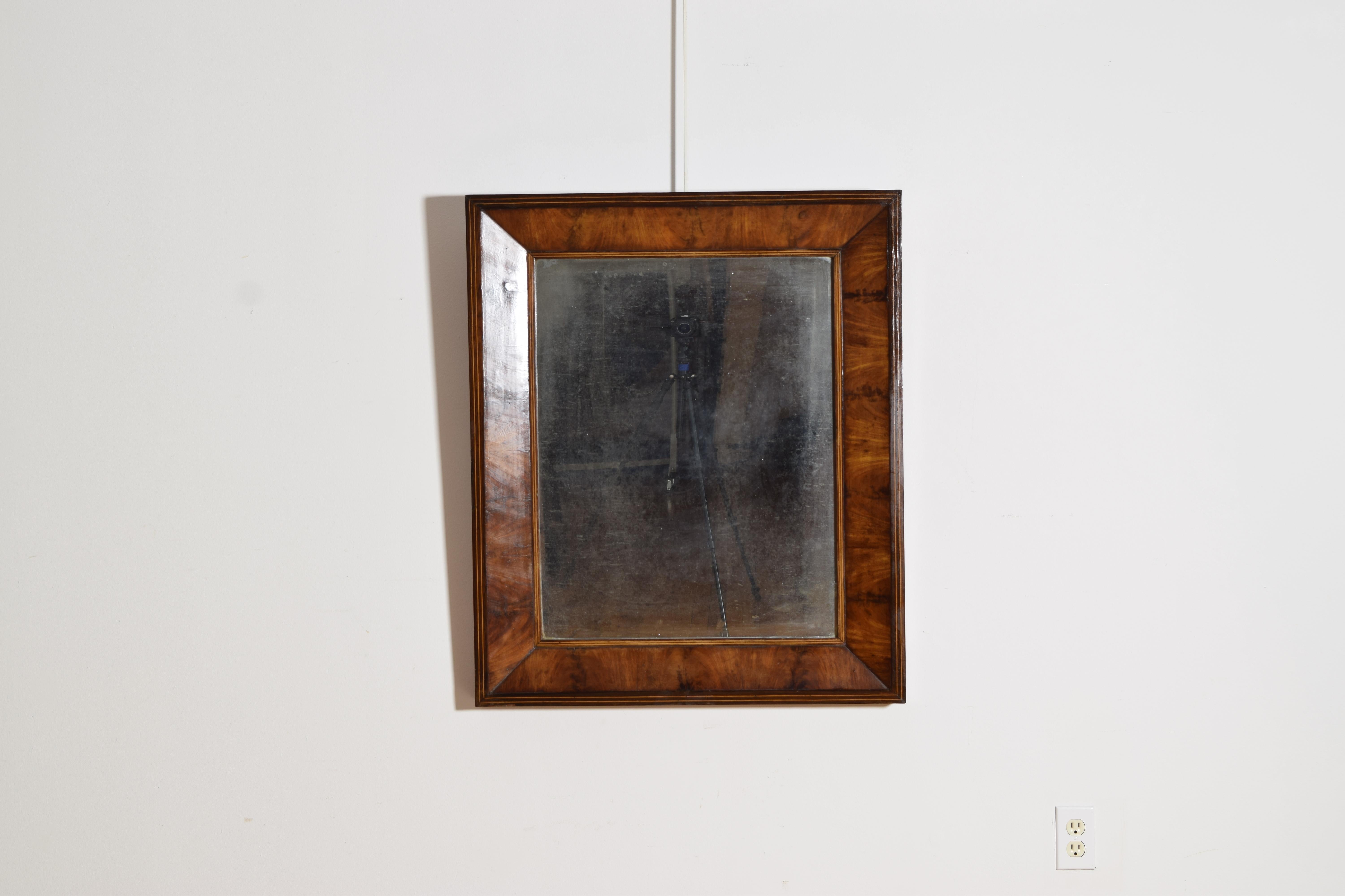 of rectangular shape with a slightly tapered concave form, the walnut veneer with band inlays at rabbet and outer edges, retaining original antique mirrorplate