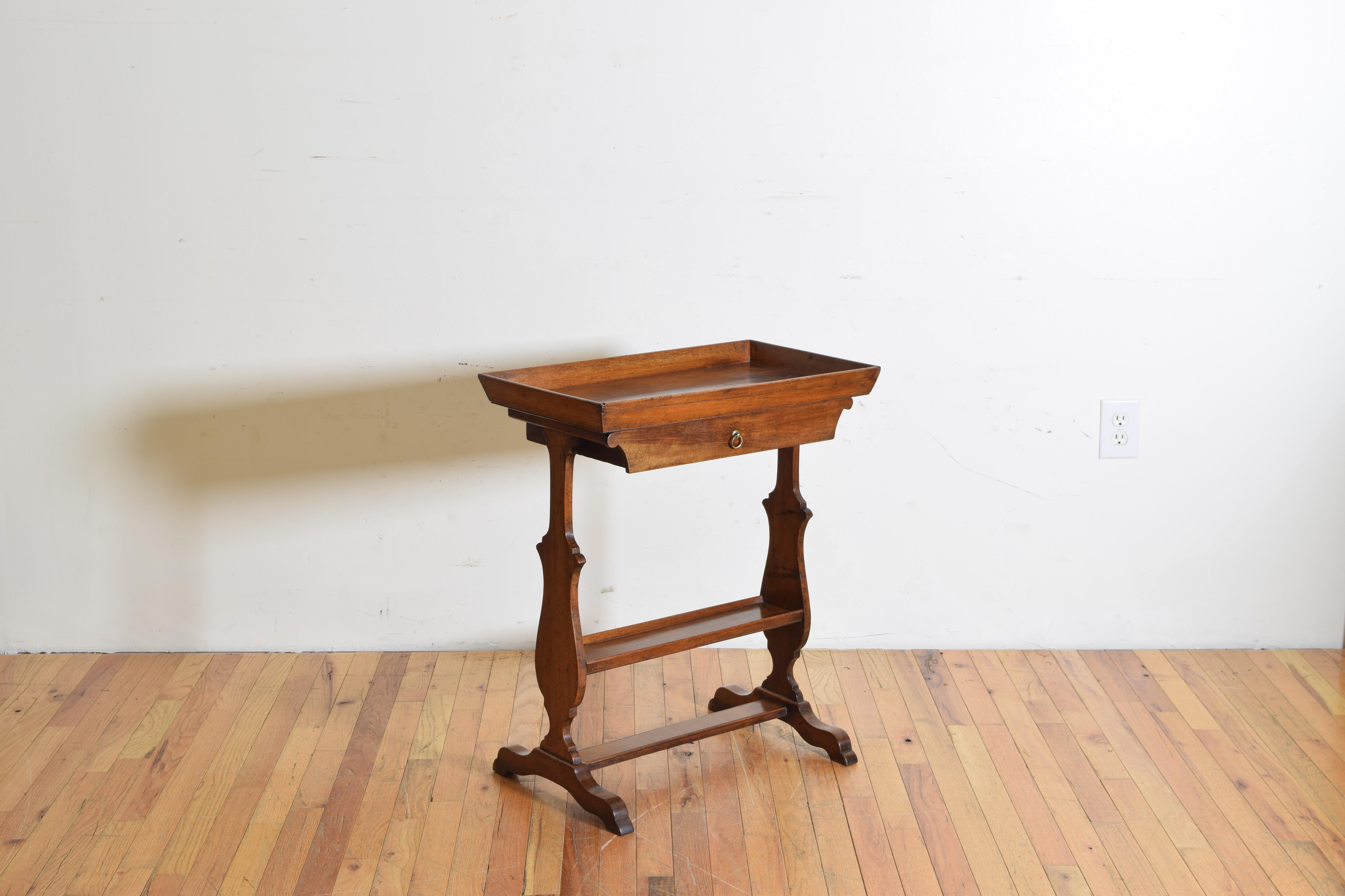 having a deep tray top above a single drawer, the shaped trestle legs joined by a centered tray with a small gallery edge, the bracket feet joined by yet another flattened stretcher, second quarter of the 19th century.