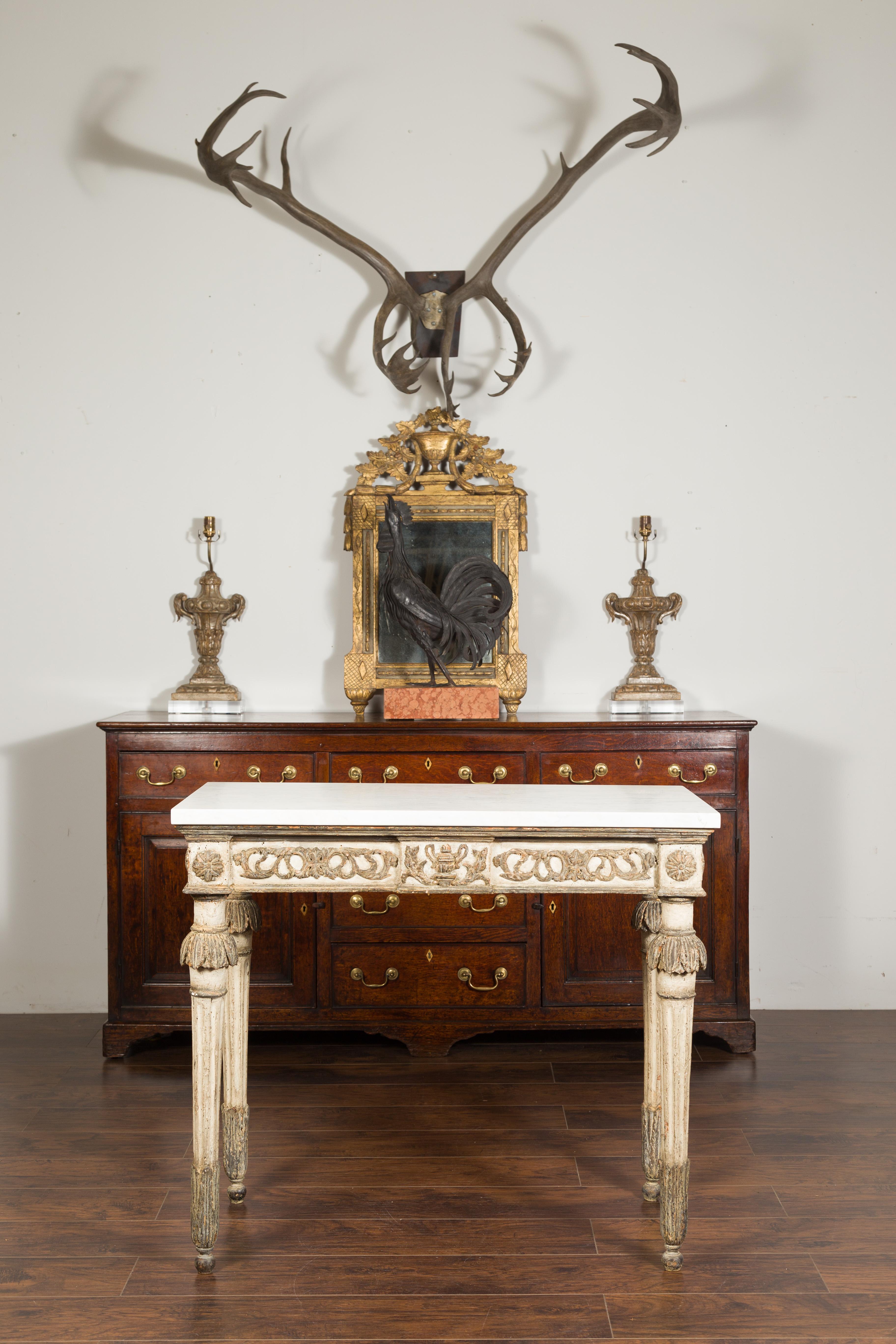 A French neoclassical period painted wood console table from the early 19th century, with white marble top, carved frieze and fluted legs. Created in France during the early years of the 19th century, this neoclassical console table features a