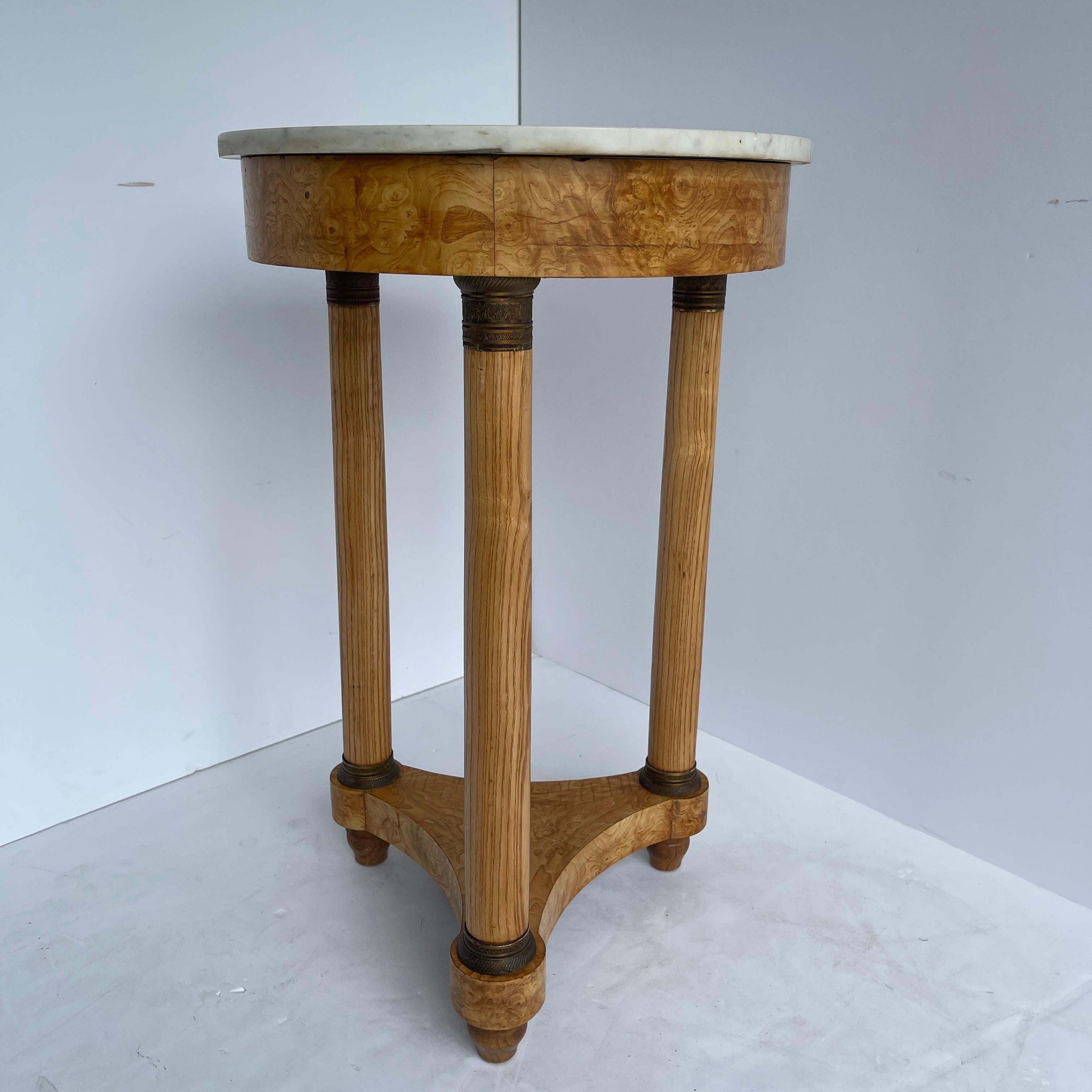 French neoclassical white marble top empire style round table with bronze hardware. Beautiful elegant maple side table with three long slender legs and lovely curved bottom trestle. The maple wood grain glows in the light. This table is perfectly
