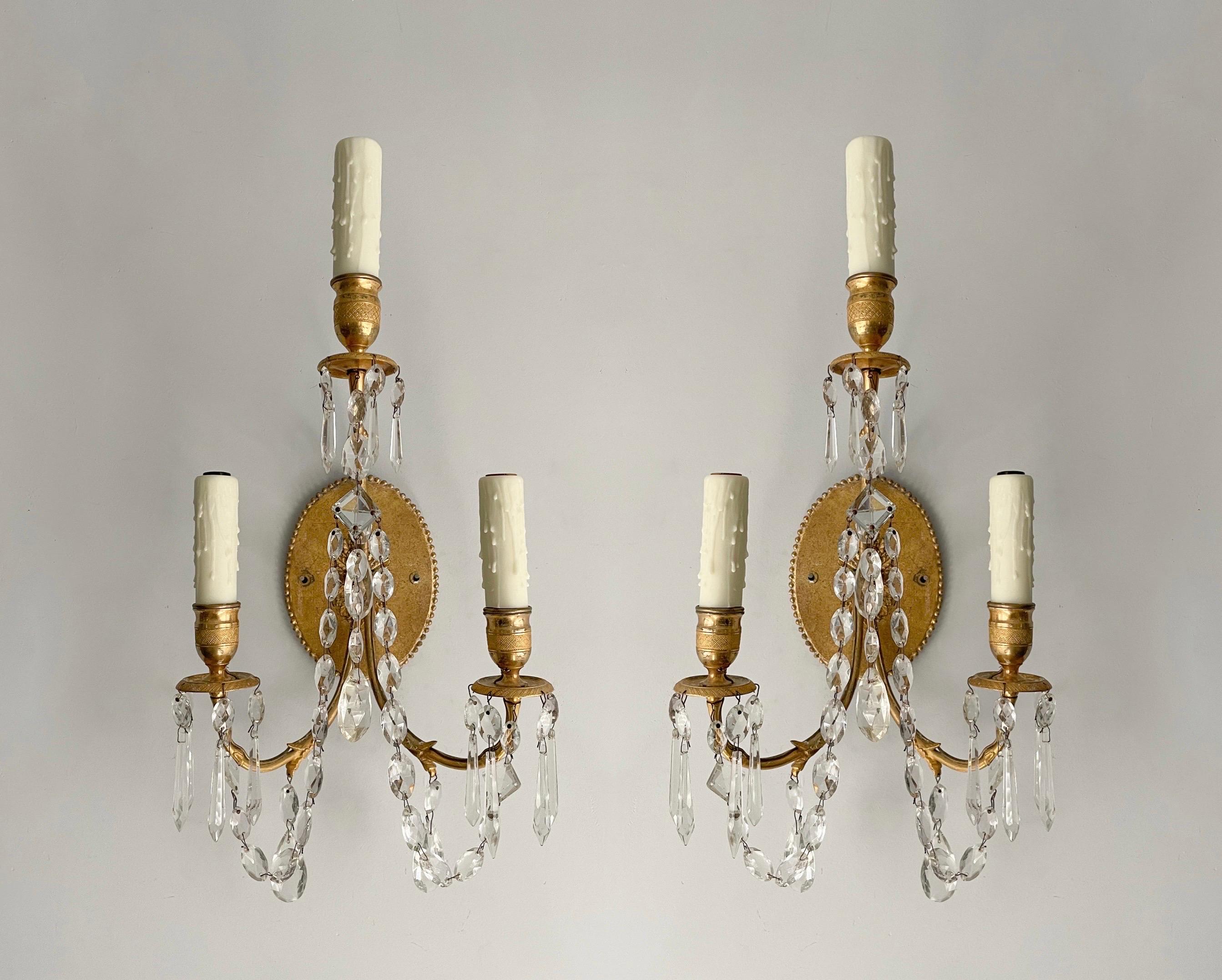 Exquisite, French 1940s pair of brass and crystal sconces in the neoclassical style, imported by Paul Ferrante, Los Angeles. 

Each sconces features a delicate gilt-brass embossed frame decorated with crystal garlands and faceted prisms.

The