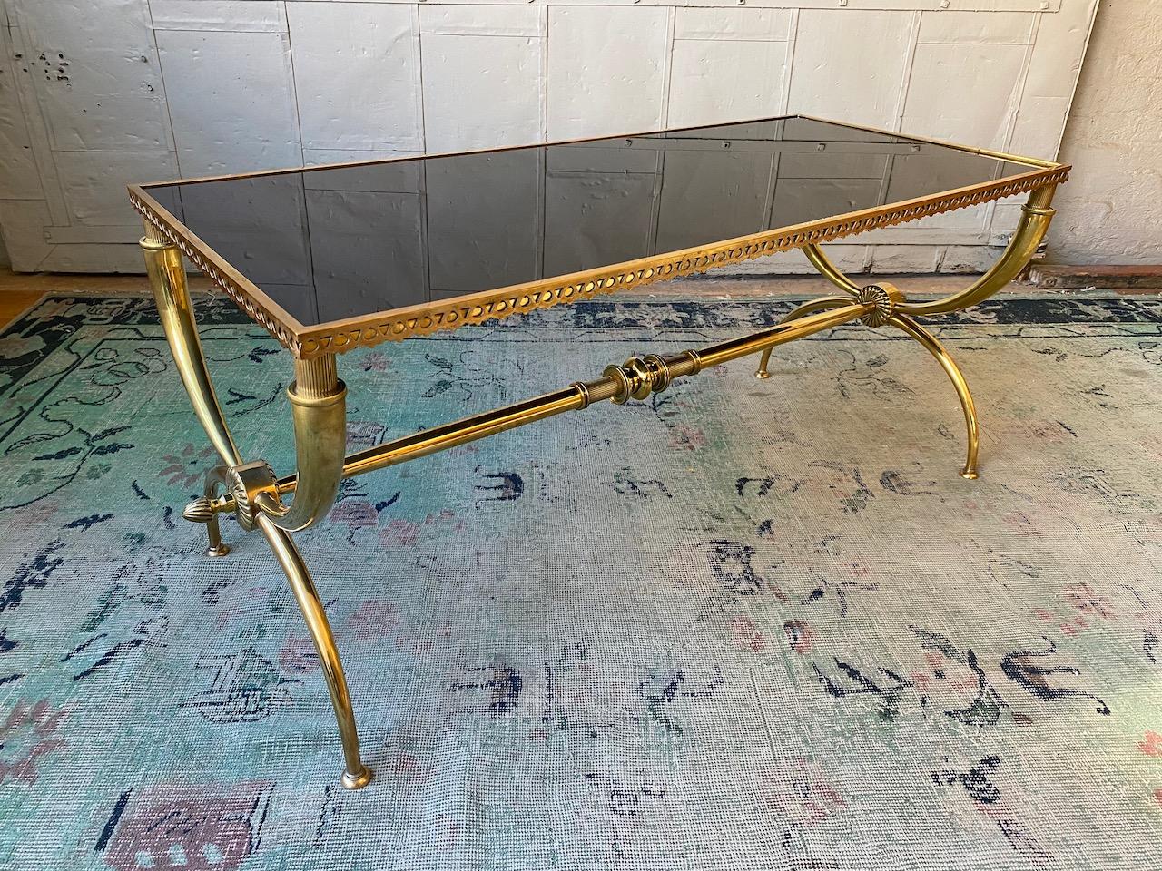 Neoclassical brass coffee table with black glass, attributed to Raymond Subes. The handsome base is comprised of both turned and cast parts, the central stretcher is flanked by curule legs. The glass is held in place by a pierced brass gallery