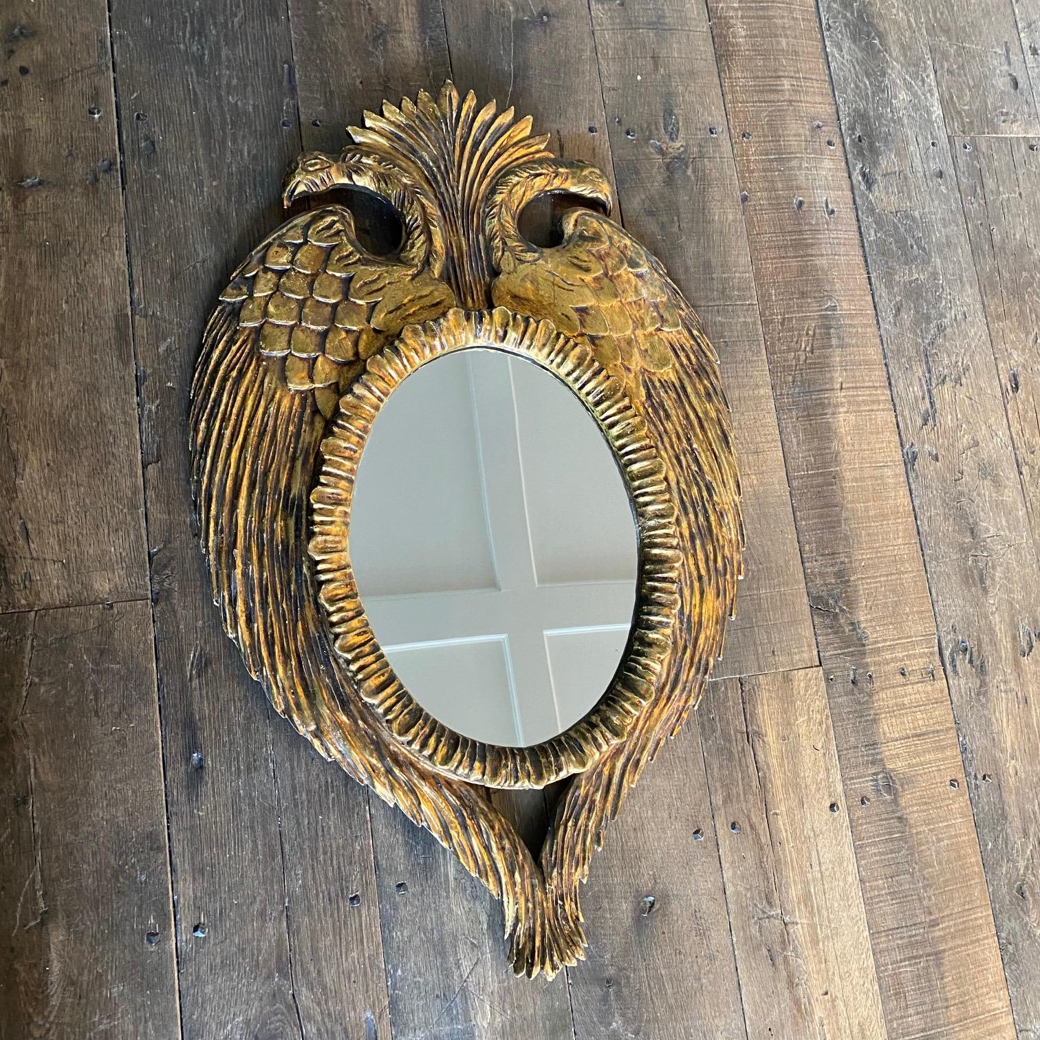 Exquisite French carved giltwood mirror frame in the form of a crowned bicephal eagle. Highly decorative frame with double-headed eagles, symmetric wings encasing the central oval mirror. This hand carved wood mirror is gilded with gold leaf, and