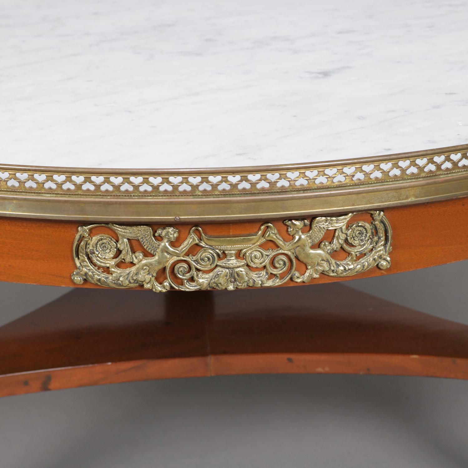 French neoclassical cocktail low table features round inset marble top seated in pierced ormolu gallery above skirt with pierced chimera and urn form ormolu mounts, raised on tripod base with lower triangular display with legs terminating in cast