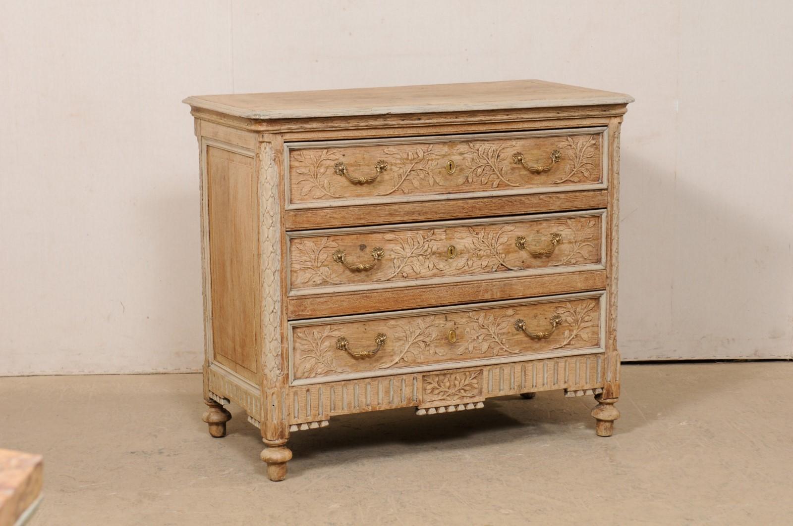 A French Neoclassical style, foliage-carved and bleached-wood chest of three-drawers from the early 19th century. This antique chest from France features a rectangular-shaped top with softly-rounded front corners, which rests atop a Neoclassic case
