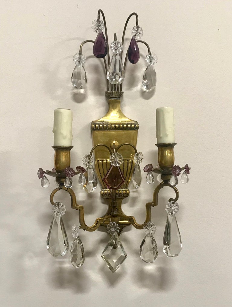 Beautiful, 1940s French brass and crystal sconces in the neoclassical style. The brass urn shaped sconces are decorated with an assortment of crystal prisms in various shapes and sizes including some In amethyst glass. Each sconce requires 2