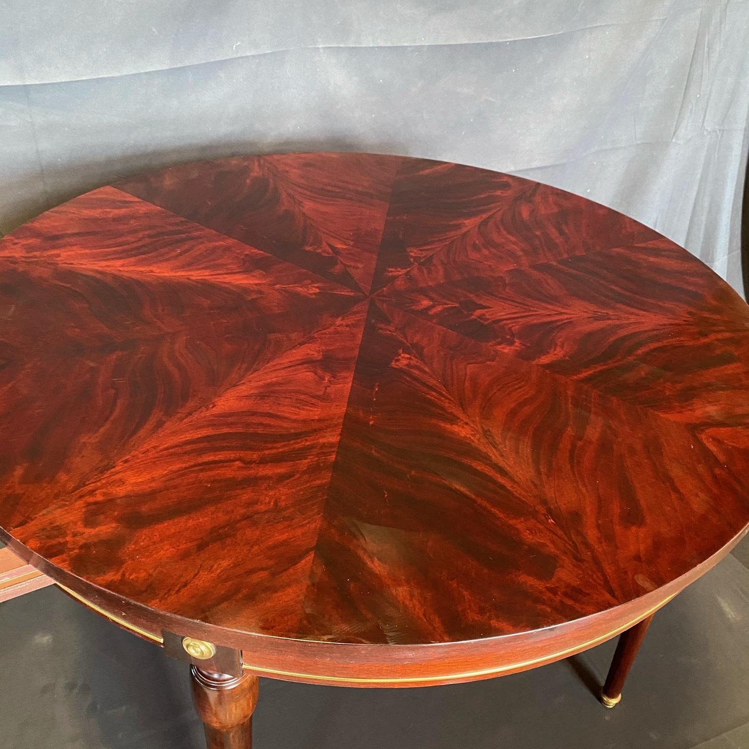 Beautiful French round mahogany and walnut table with gold accents having gold pulls on either side that extend if leaves are desired (not included). Bought in Lyon, France, this table has a stunning burled top. Very versatile size to be used as a