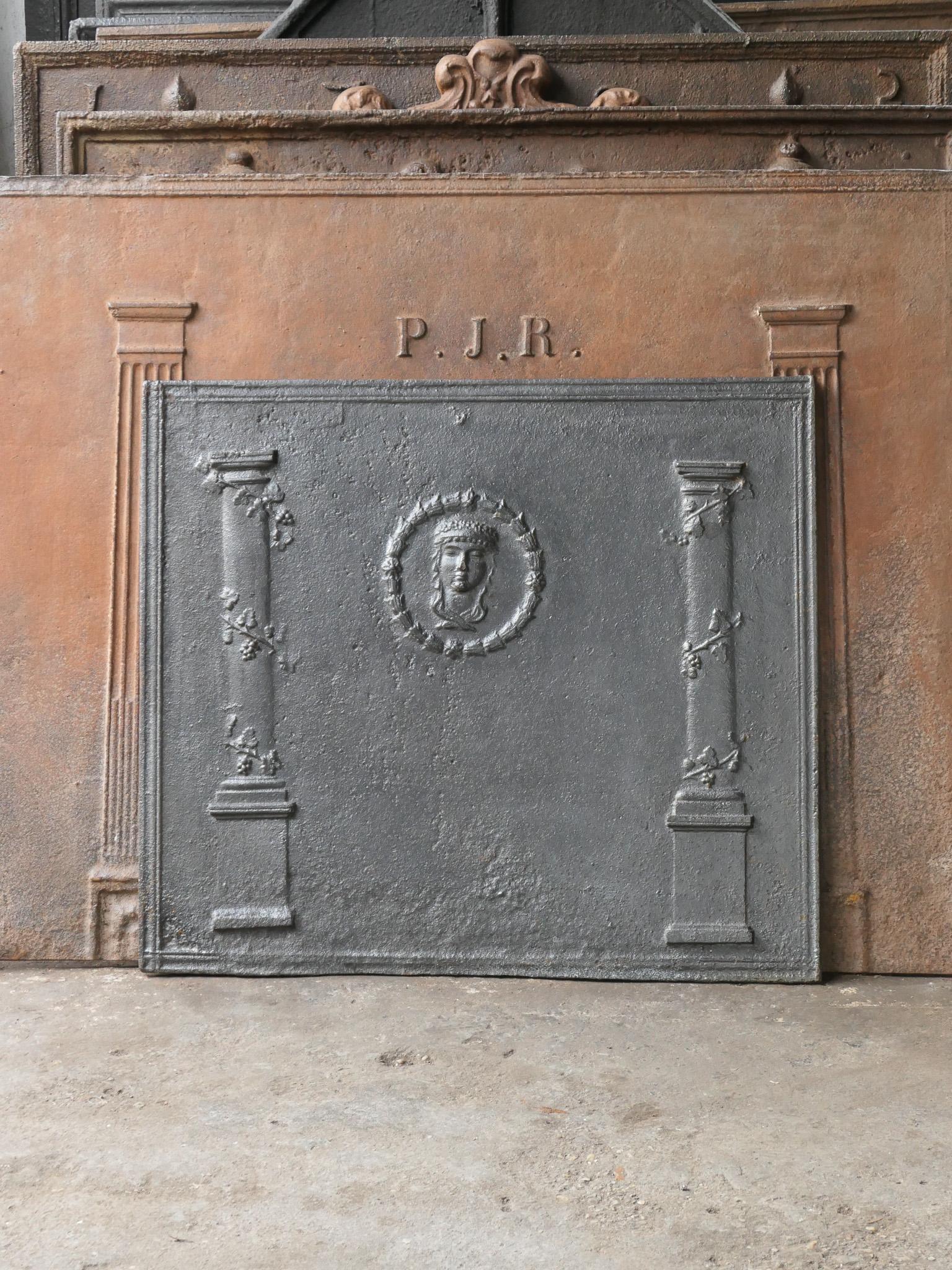 18th - 19th century French neoclassical fireback with two pillars surrounded by wine tendrils. The 'pillars of freedom' symbolize the value liberty, one of the three values of the French revolution. In the center is a decoration of a face of unknown
