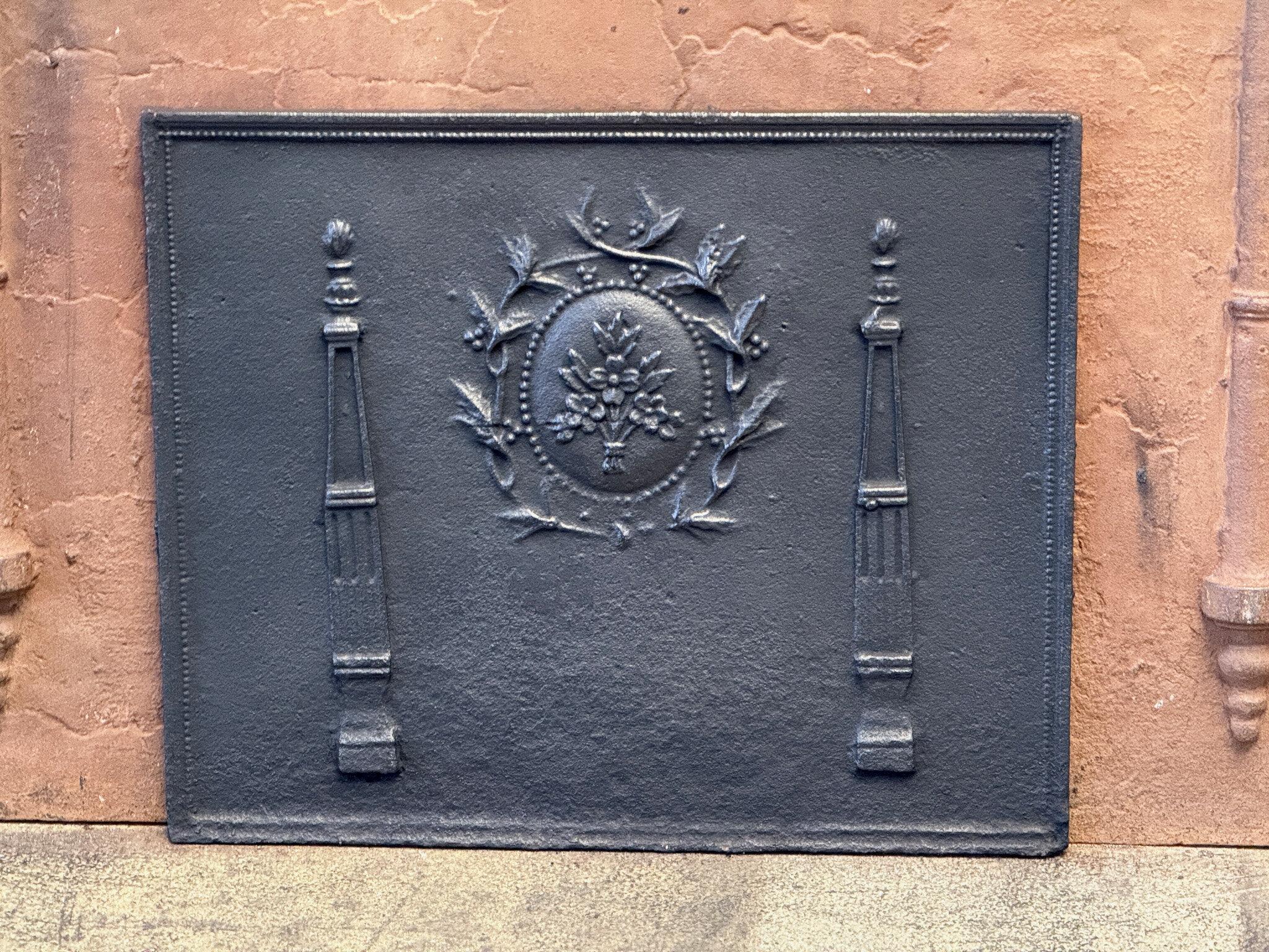French Neoclassical Period fireback with two pillars and a floral decoration.

The fireback is made of cast iron and has a black/pewter color. It is in good condition and does not have cracks.