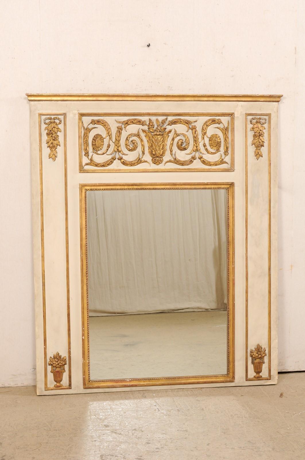 A French large-sized neoclassic mirror from the 19th century. This antique mirror from France is beautifully embellished with traditional Neoclassical carved elements including scrolling foliage, bow-tie topped hanging garlands, and urns with floral