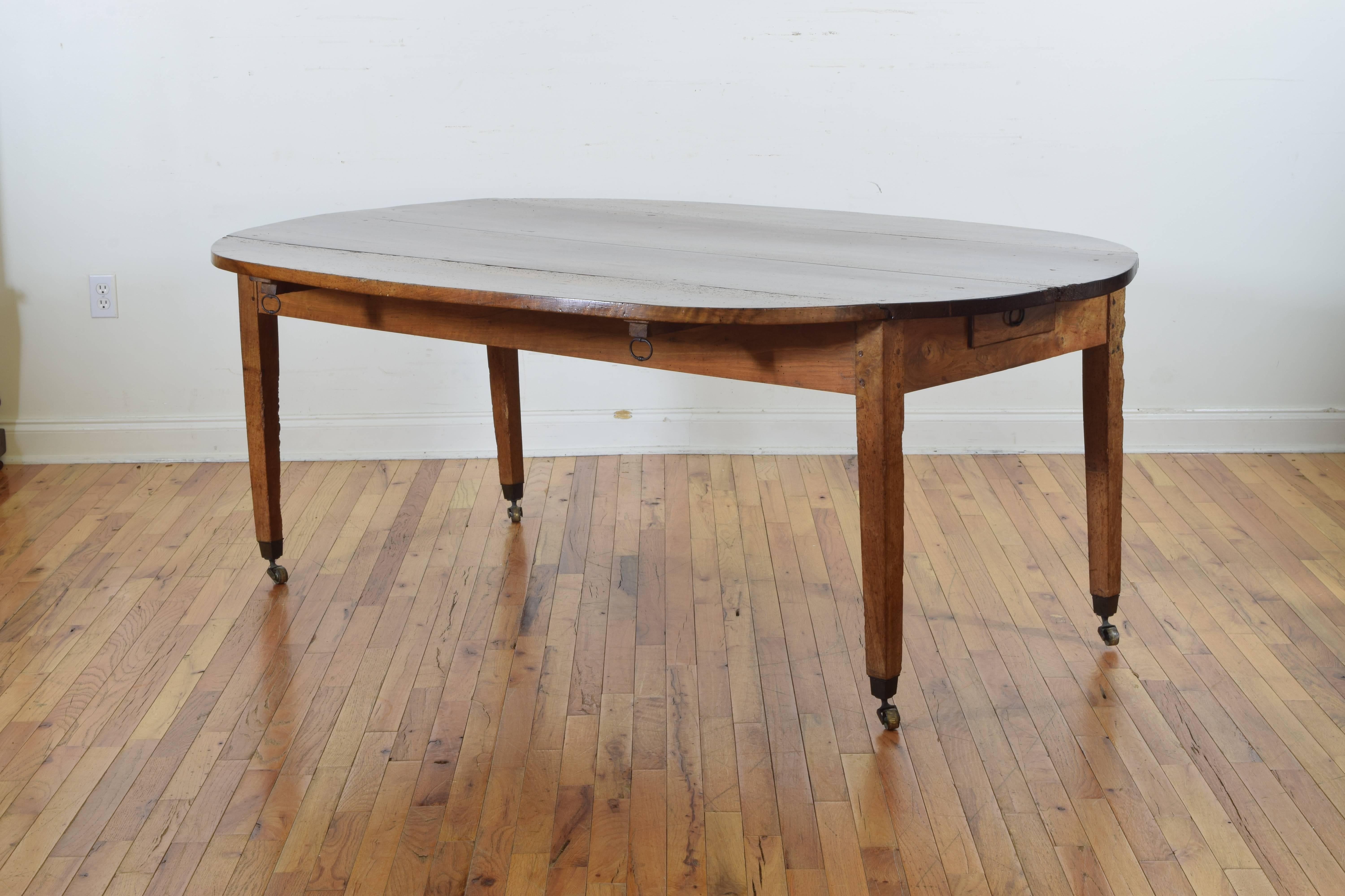 The rectangular top flanked by two drop leaves when extended forming an elongated oval, the case housing one drawer and four pull-out supports for leaves, raised on square tapering legs with original brass castors, listed measurements are for table