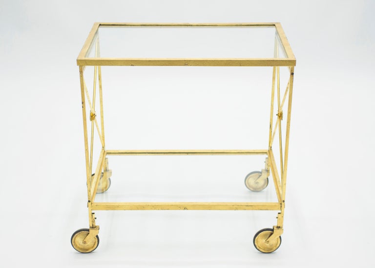 This chic bar cart from the 1960s carries with it the elegant mood of the neoclassical post Art Deco period. Glittering in an antiqued gold gilt finish, this iron craft bar cart adds a glam twist which makes a gracious compliment to both traditional