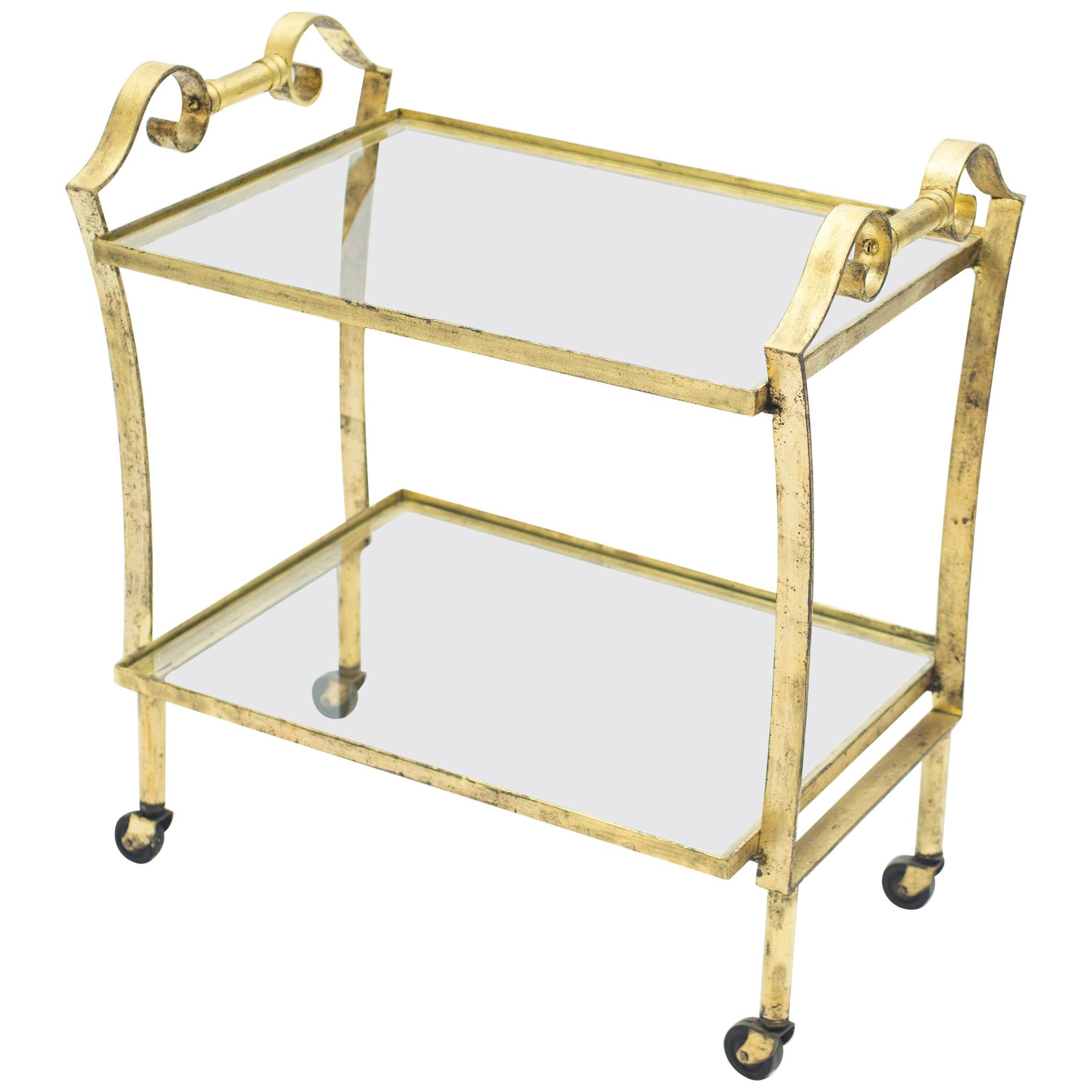 This chic bar cart from the 1940s carries with it the elegant mood of the neoclassical post Art Deco period. Glittering in an antiqued gold gilt finish, this iron craft bar cart adds a glam twist which makes a gracious compliment to both traditional