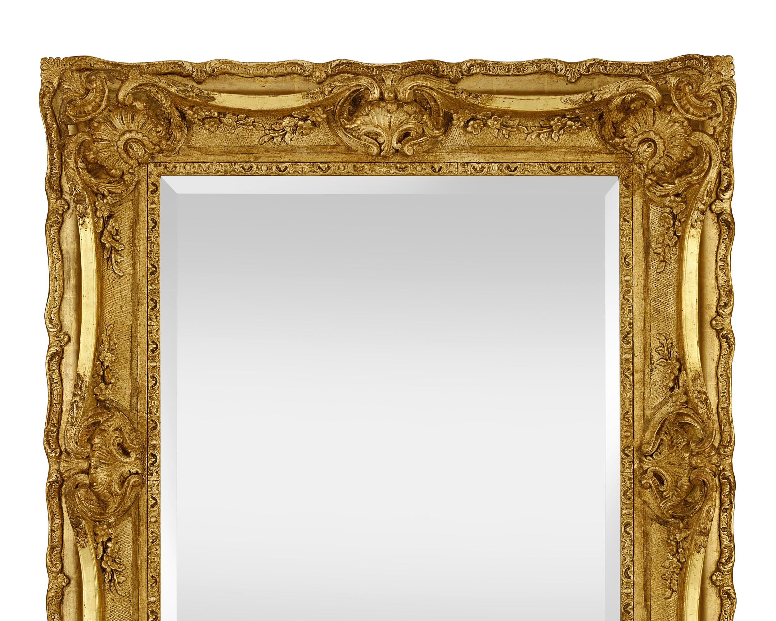 This beautiful mirror is ornately carved in the Louis XIV style. Period motifs including scrolls, shells and trailing foliage adorn the giltwood frame that surrounds the beveled glass mirror. Overall, its intricate craftsmanship, large size and