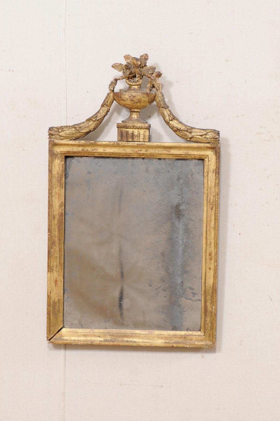 A French Neoclassical mirror from the turn of the 18th and 19th century. This antique mirror from France has a rectangular-shaped mirror within a carved gilt wood surround, and in typical Neoclassical style, has a carved and raised urn crest atop of