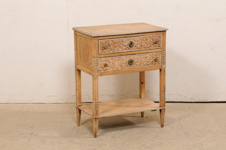 A French neoclassical style raised two-drawer side chest, with lower shelf, from the 19th century. This antique small-sized commode from France has a rectangular-shaped top with rounded corners, atop a case which house two drawers, and raised upon