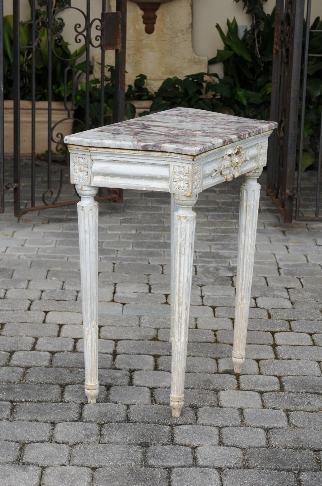 A French neoclassical period painted wood console table from the early 19th century, with marble top, carved apron and fluted legs. Born in post-revolution France during the early years of the 19th century, this exquisite painted console table