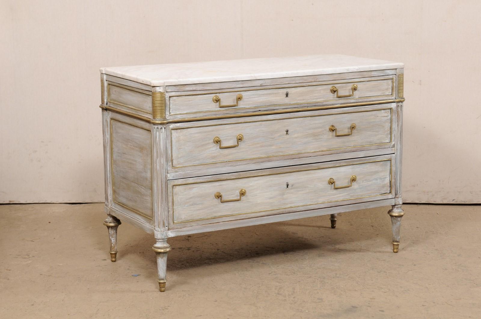 A French period Neoclassical commode with brass accents from the early 19th century. This antique chest from France features a rectangular-shaped marble top, with pronounced rounded corners at front, which rests atop a neoclassical case with rounded