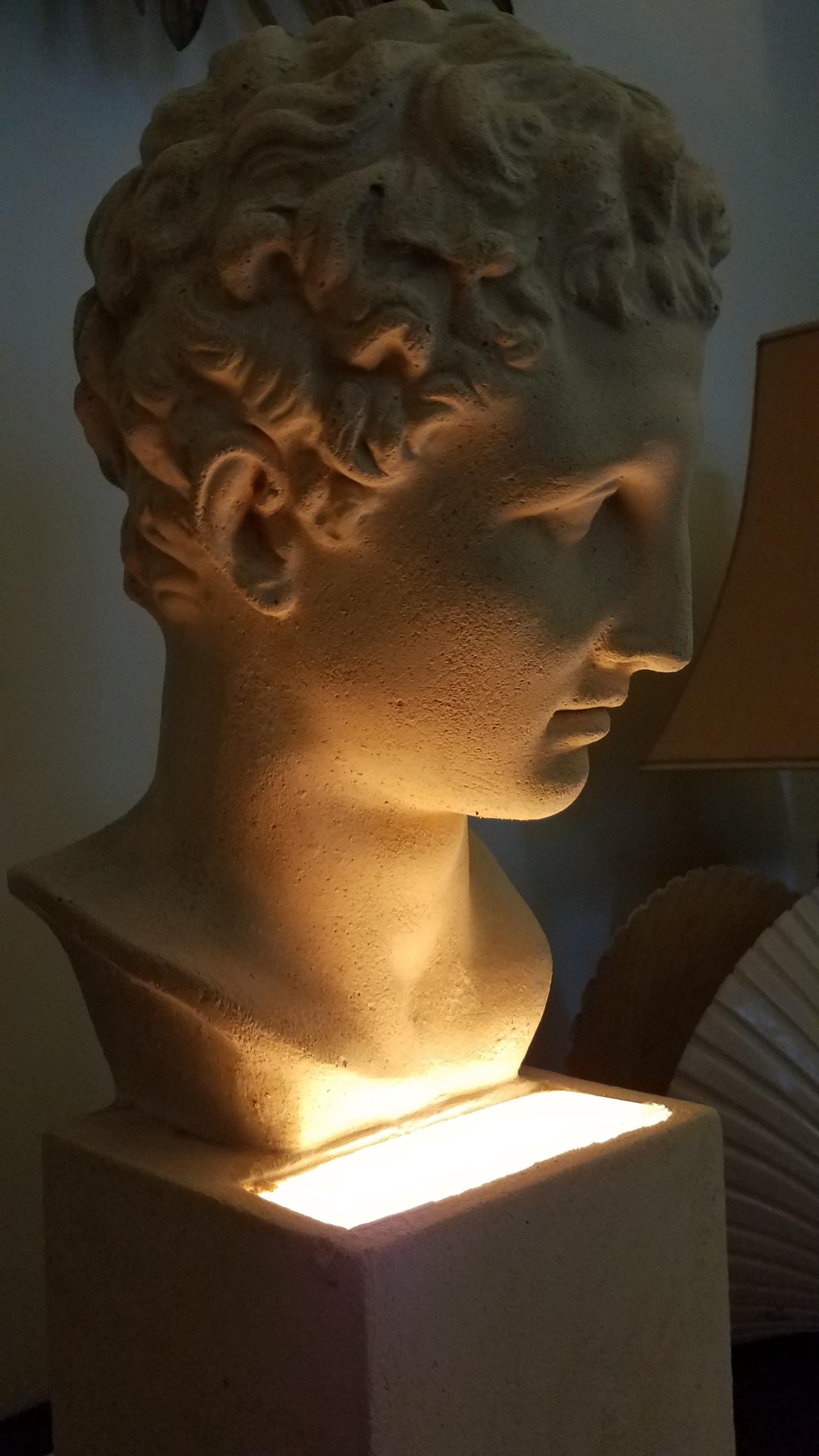 1970s neoclassical revivalist lamp made of plaster. The base is the bust of a young man in the French Neoclassical style. The light is set into its mount to illuminate the bust from below.  
