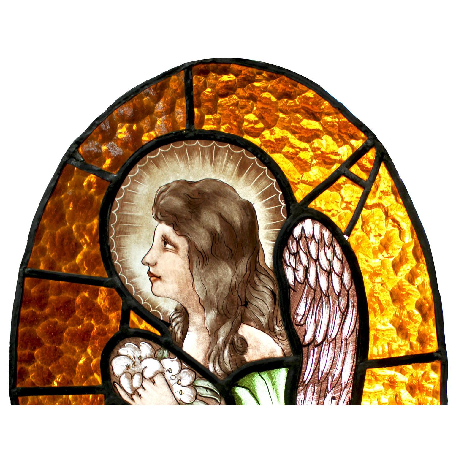A French early 20th Century Neoclassical Revival stained glass panel depicting a praying angel or cupid. The charming oval shaped hand-painted multi-colored glass panel or window depicting a side view of a praying angel or cupid, a holy halo over