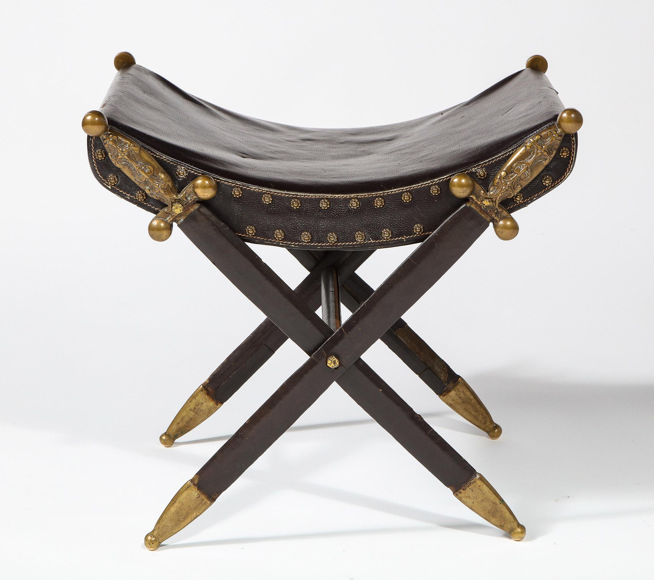 The bench with a patent leather seat and brass rosette nailheads supported by crossed swords embossed with Fleur de Lis handles and constructed of steel and brass.