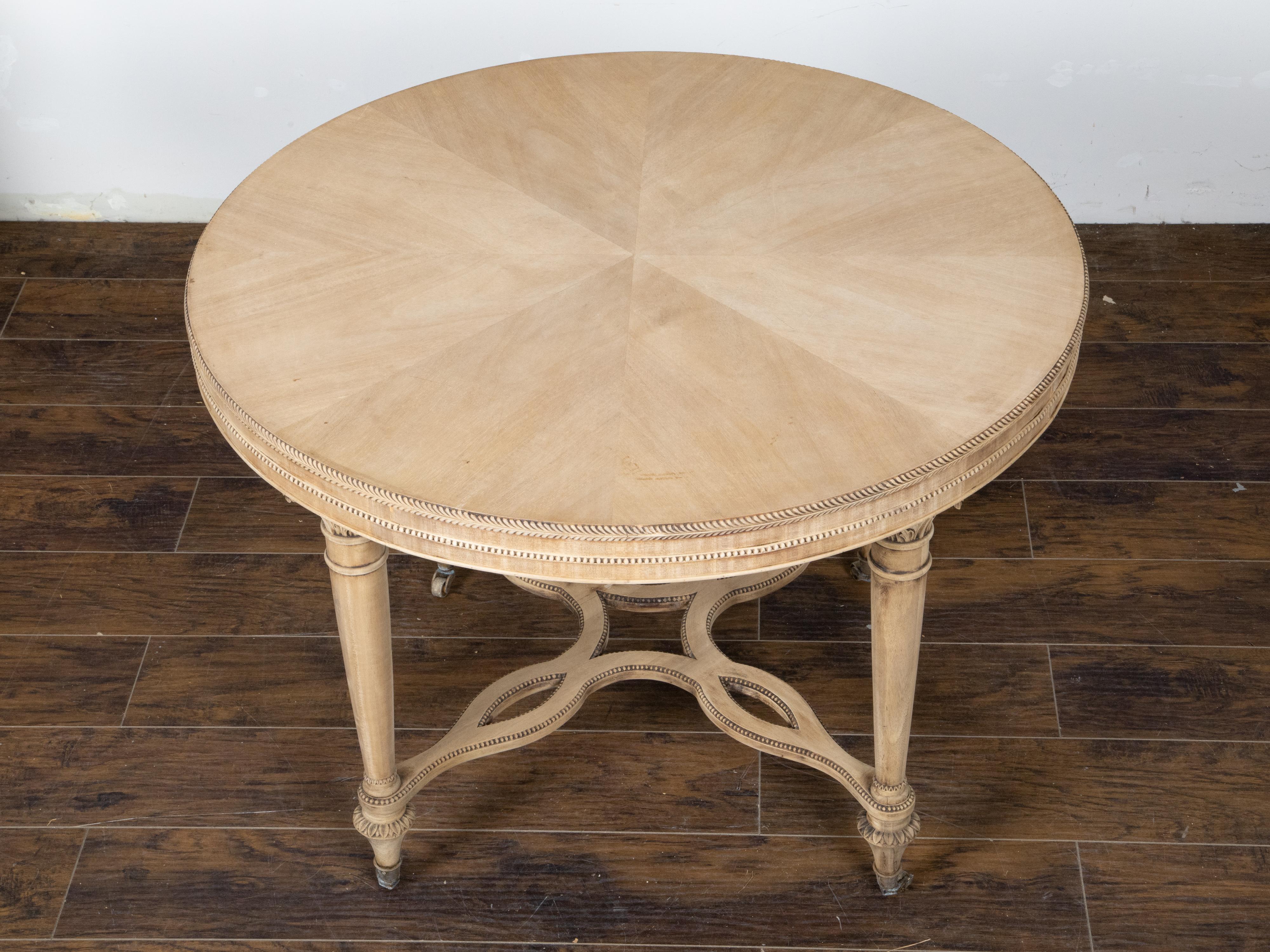 A French neoclassical style bleached walnut center table from the early 20th century with round top, carved column legs and X-Form cross stretcher. Created in France during the first quarter of the 20th century, this center table showcases the