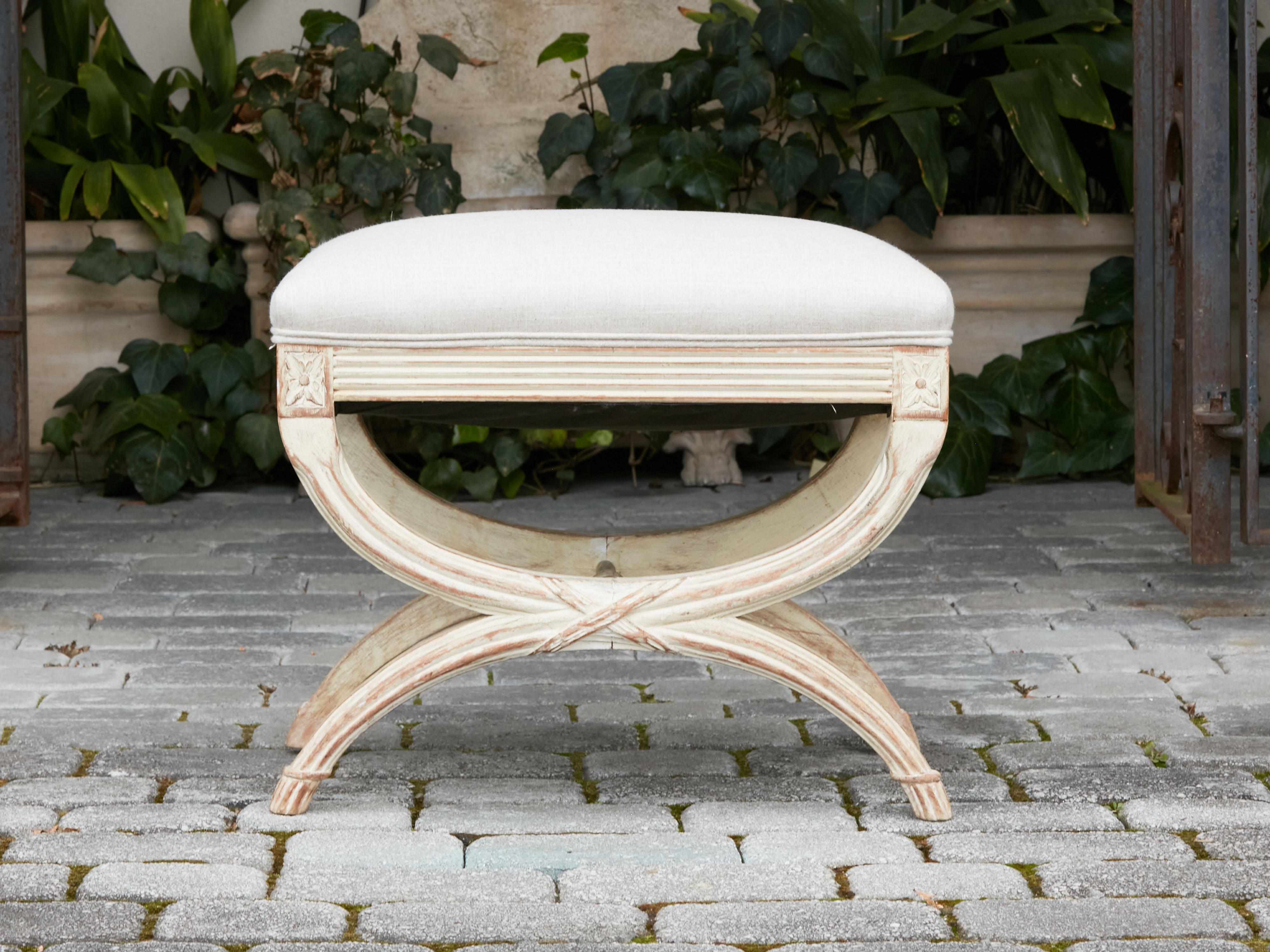 A French Neoclassical style curule painted wood stool from the early 20th century, with double X-Form base and new upholstery. Created in France during the second quarter of the 20th century, this curule stool features a rectangular seat newly