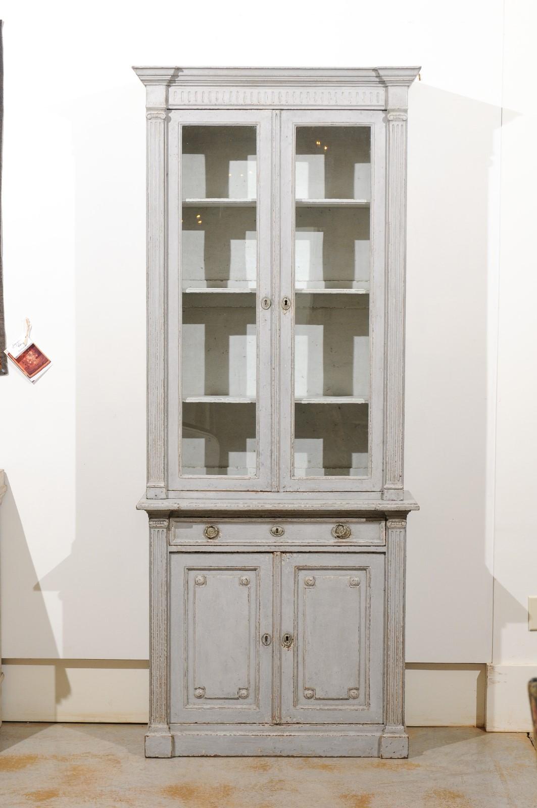 Two French neoclassical style tall painted two-part bookcases from the 19th century, with glass doors, long drawer and fluted motifs, priced and sold separately. Each of these two tall French bibliothèques features a molded cornice sitting above a