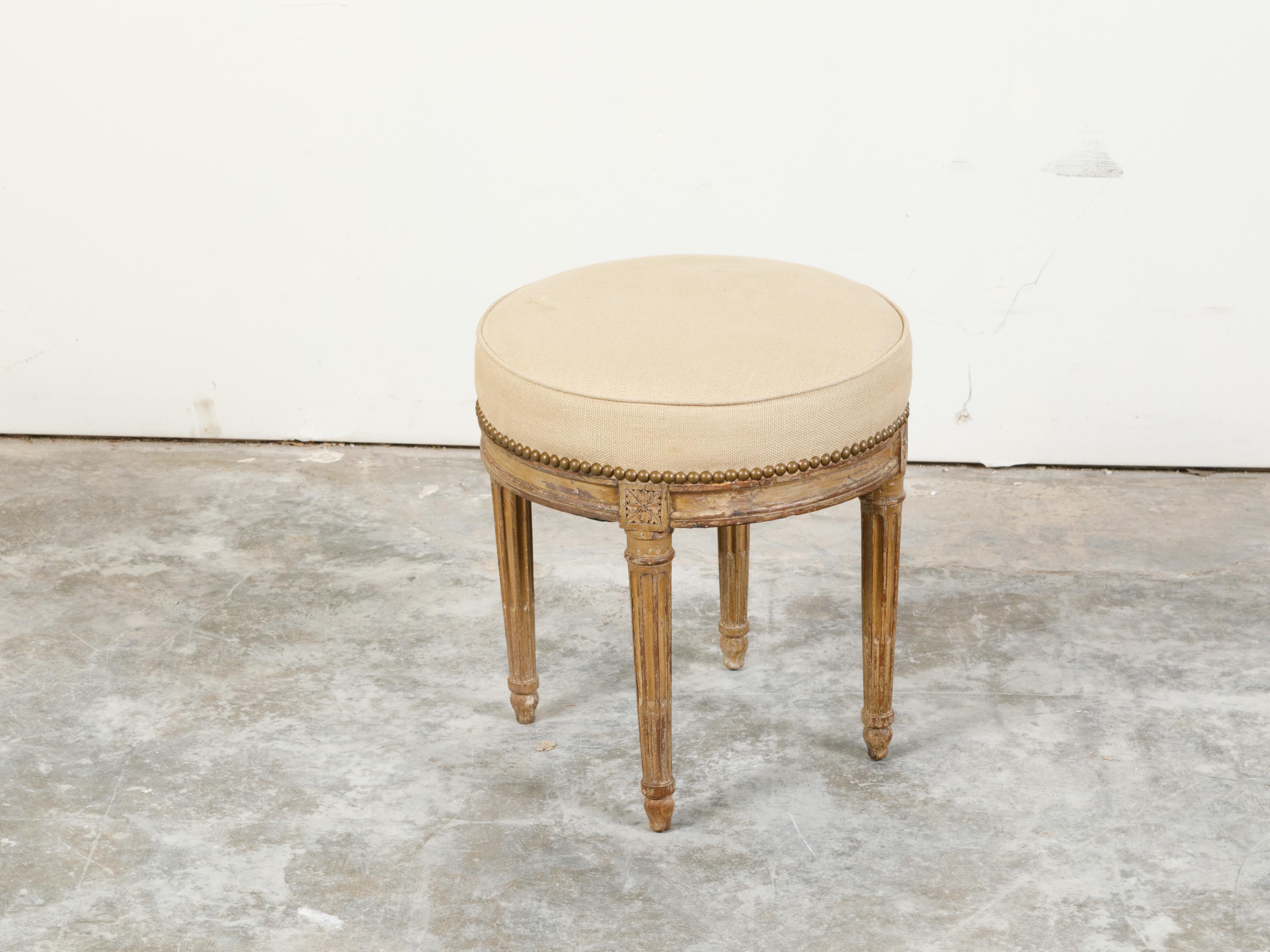 A French Neoclassical style painted wood stool from the 19th century, with fluted legs and new upholstery. Created in France during the 19th century, this Neoclassical style stool features a circular top newly recovered with a neutral toned fabric