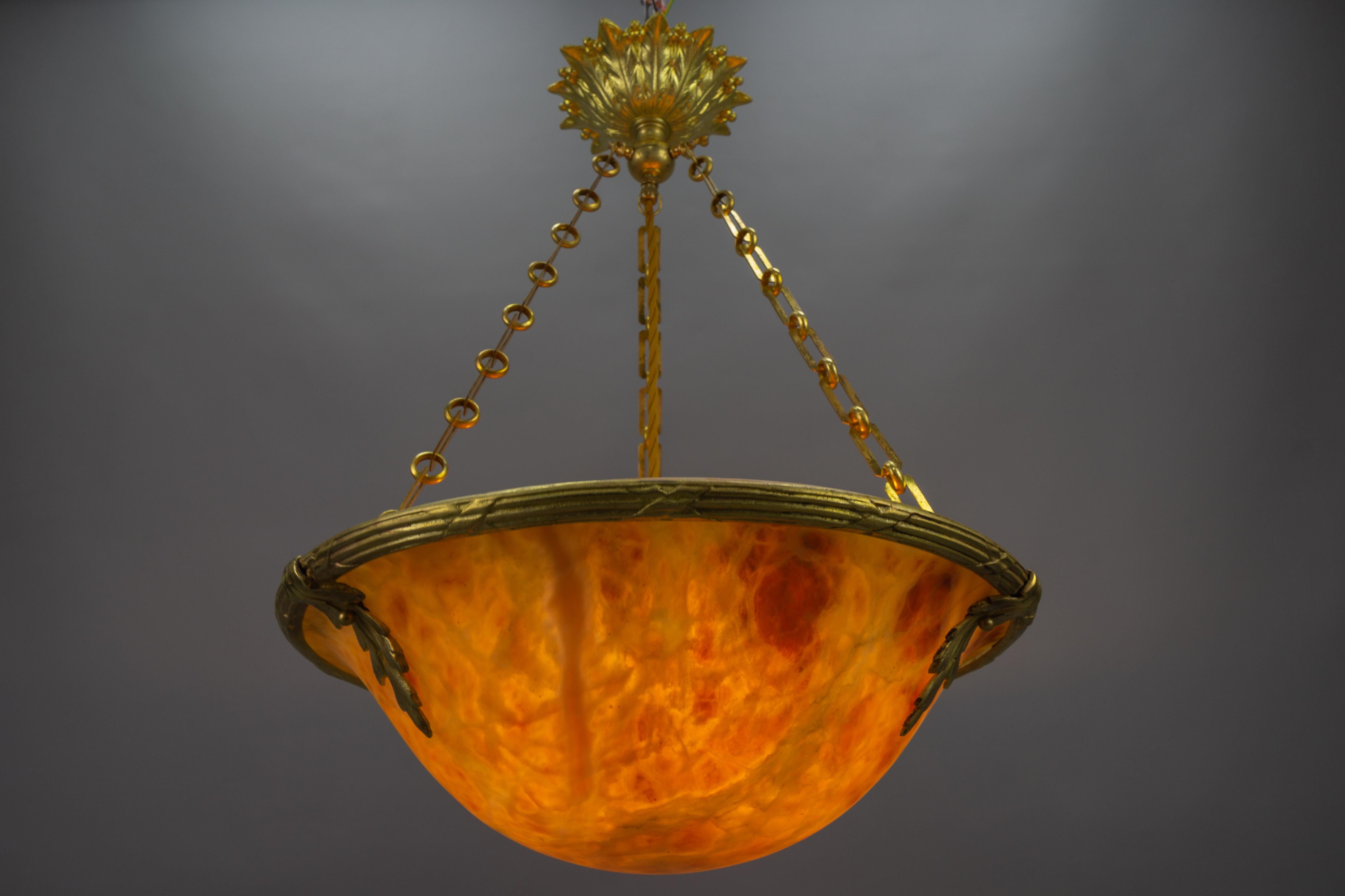 A magnificent Neoclassical style amber color alabaster pendant ceiling light fixture with an ornate bronze frame. France, 1920s. 
This masterfully carved beautiful alabaster bowl is held by a bronze rim with leaf-shaped attachments and suspended by