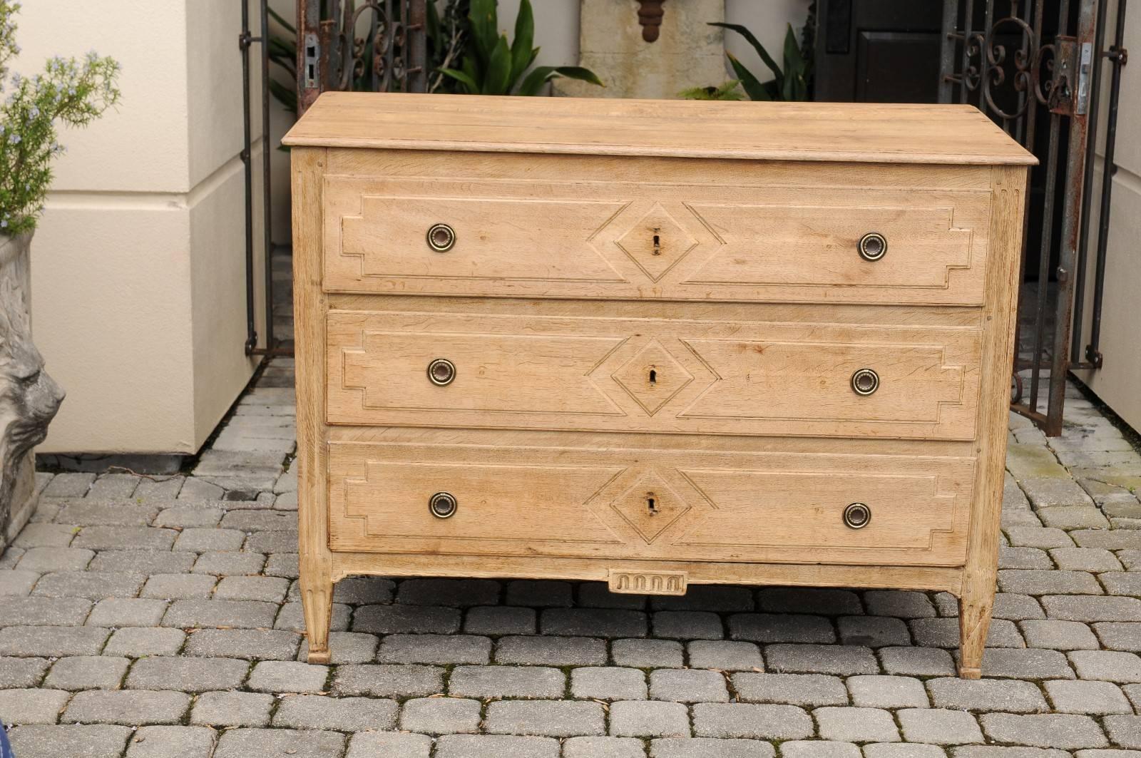 A French bleached oak neoclassical style three-drawer commode with diamond motifs from the mid-19th century. This French oak commode features a rectangular planked top sitting above three drawers with geometrical motifs carved in low-relief. Two