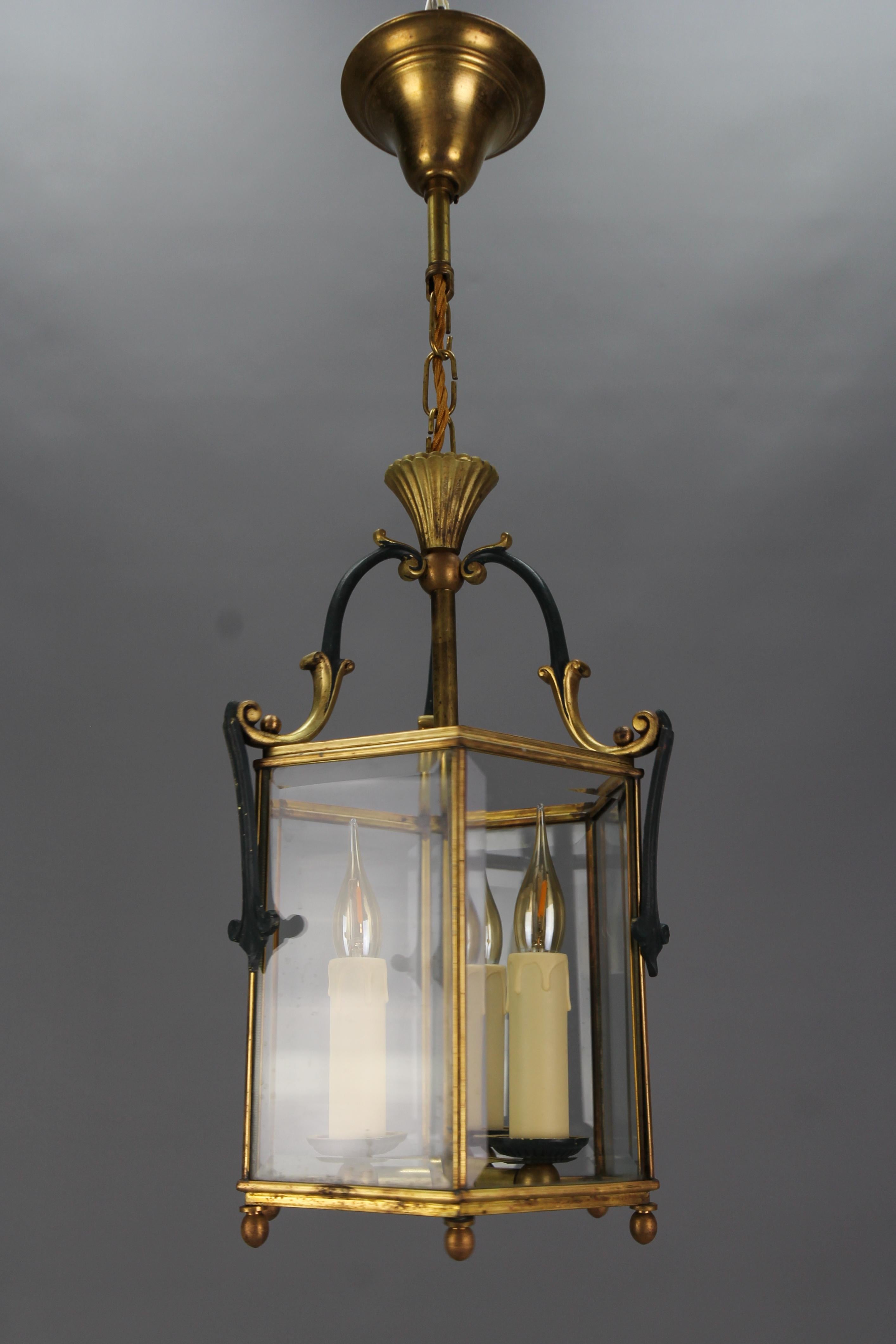 French brass and beveled clear glass hexagonal hanging lantern from circa the 1920s.
This adorable three-light antique pendant lantern features an elegant hexagonal brass frame with dark green painted details and six slightly beveled clear glass
